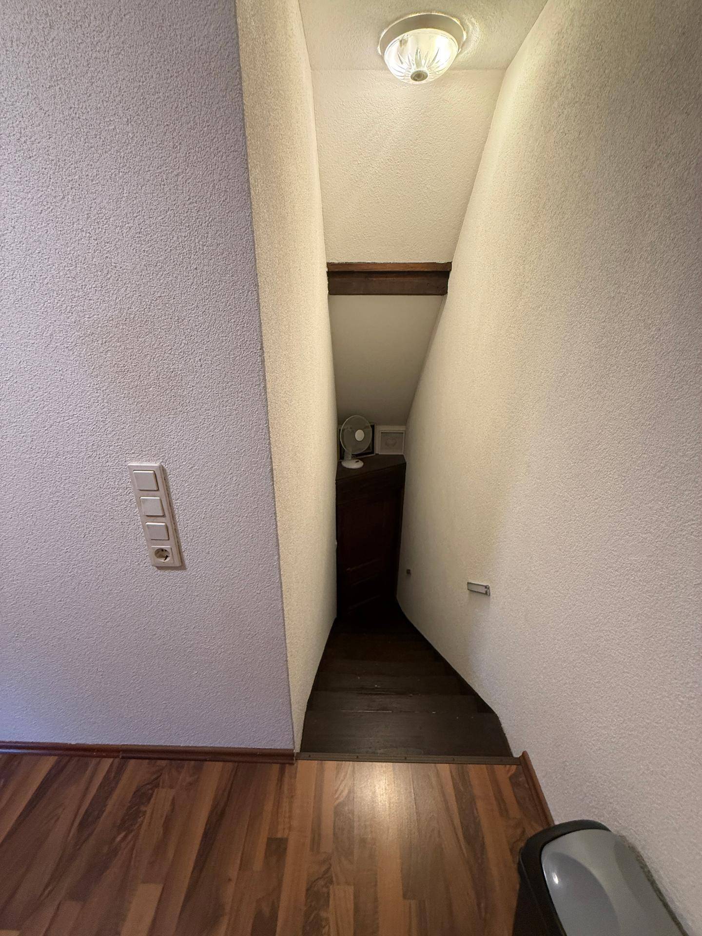 Schmale Treppe mit Holzfußboden und strukturierten Wänden, die in einen unteren Bereich führt.