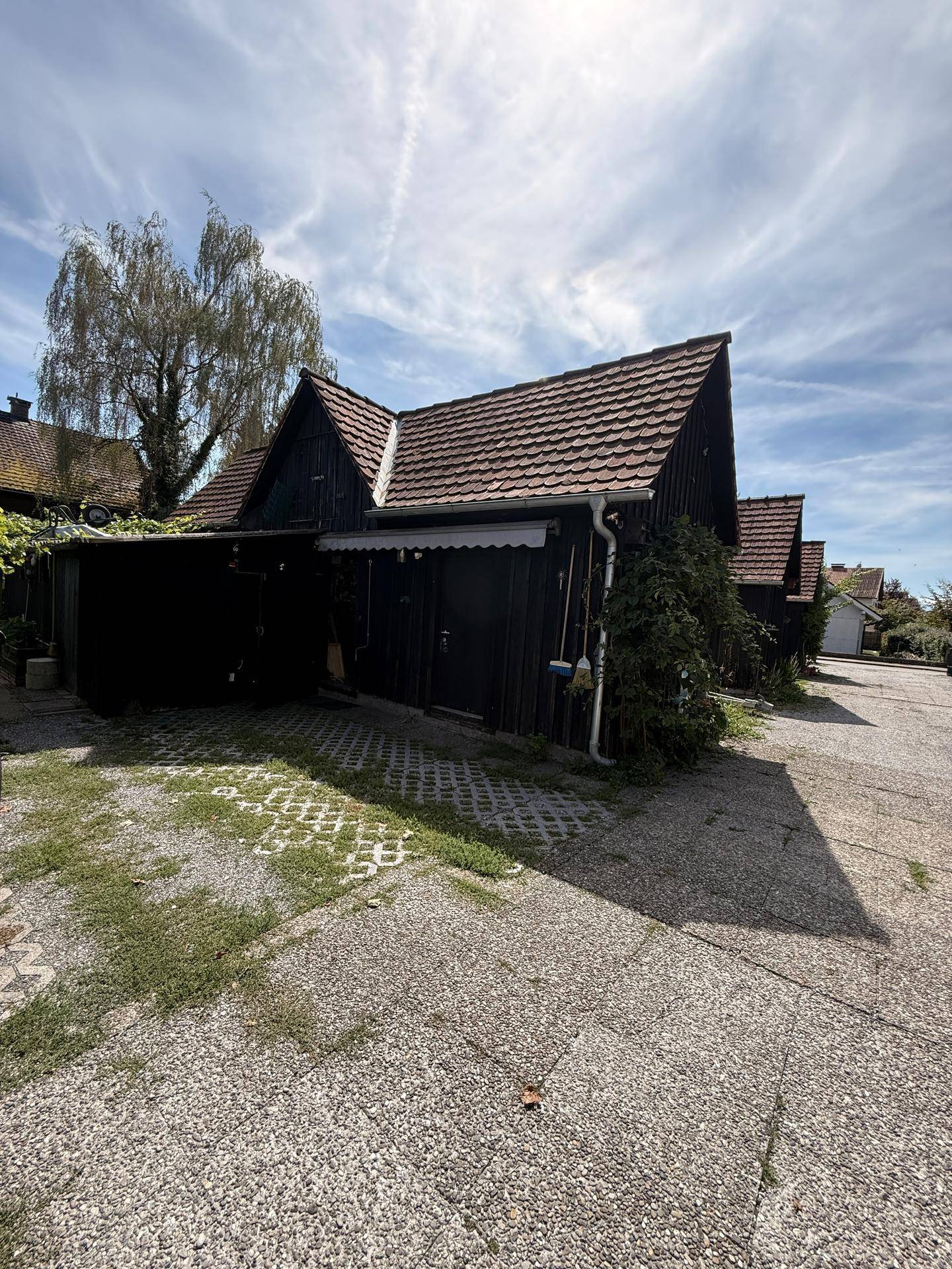 Reihe von dunklen Holzschuppen oder Garagen mit Satteldächern und einem gepflasterten Vorplatz.