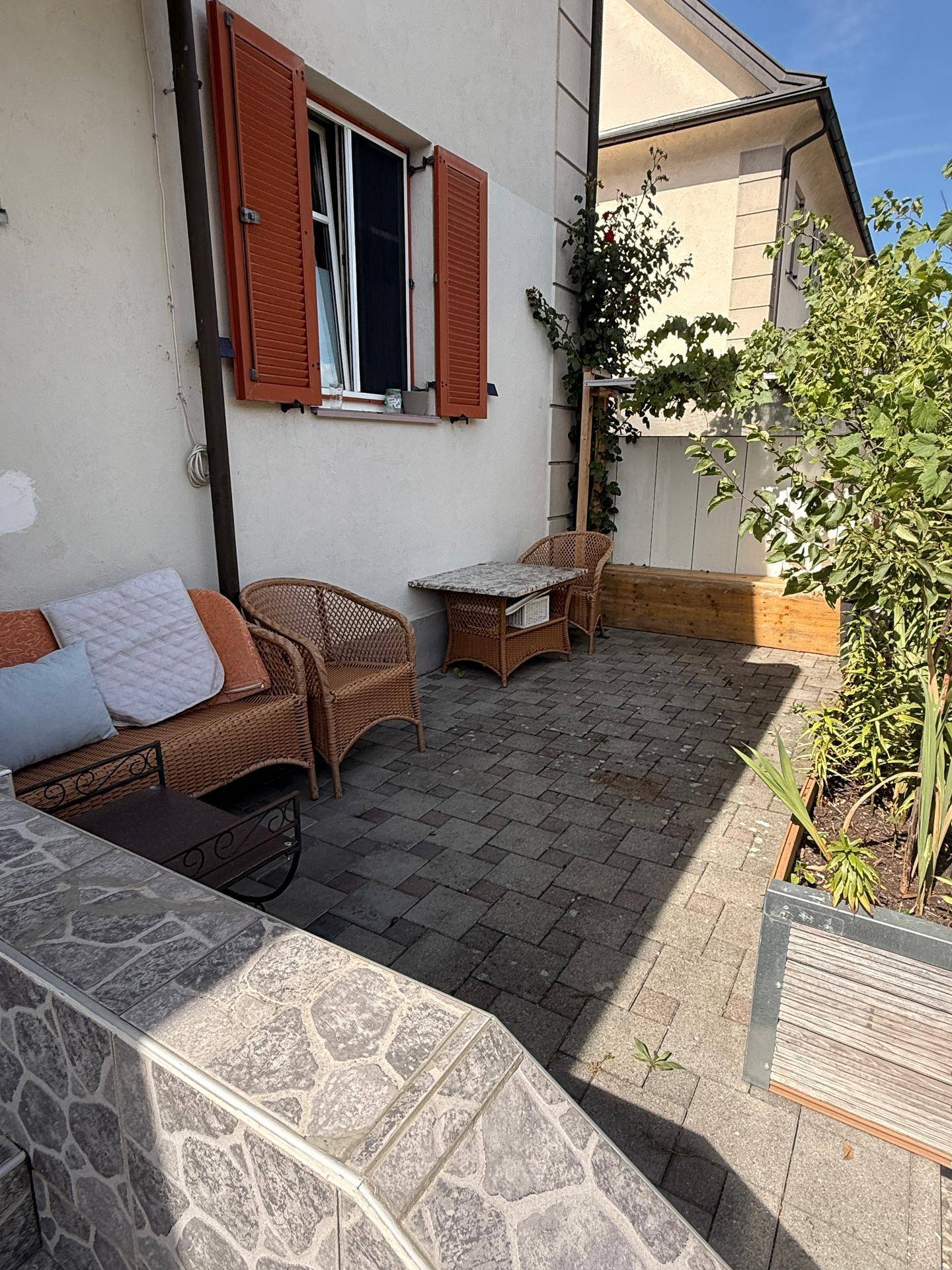 Gemütliche kleine Terrasse mit Korbmöbeln und Topfpflanzen, ideal für entspannte Stunden im Freien.