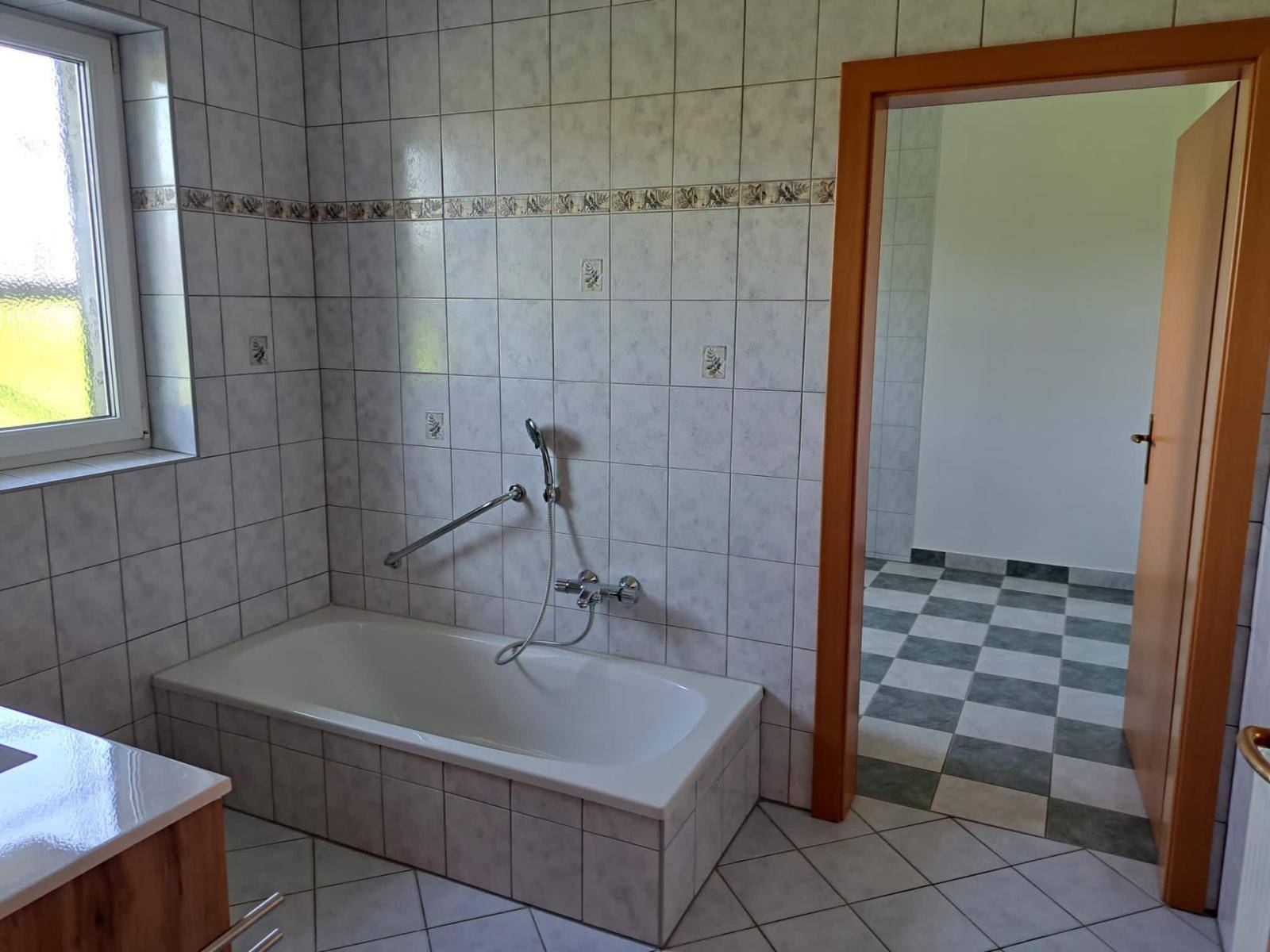 Badezimmer mit Badewanne, Wandfliesen und Fenster, bereit zur individuellen Gestaltung.