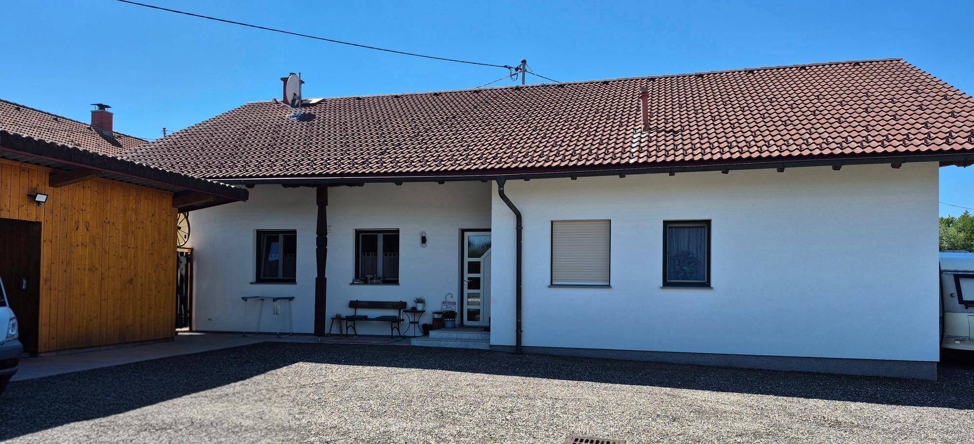 Vorderansicht des Einfamilienhauses mit Zufahrt und Carport unter strahlend blauem Himmel.