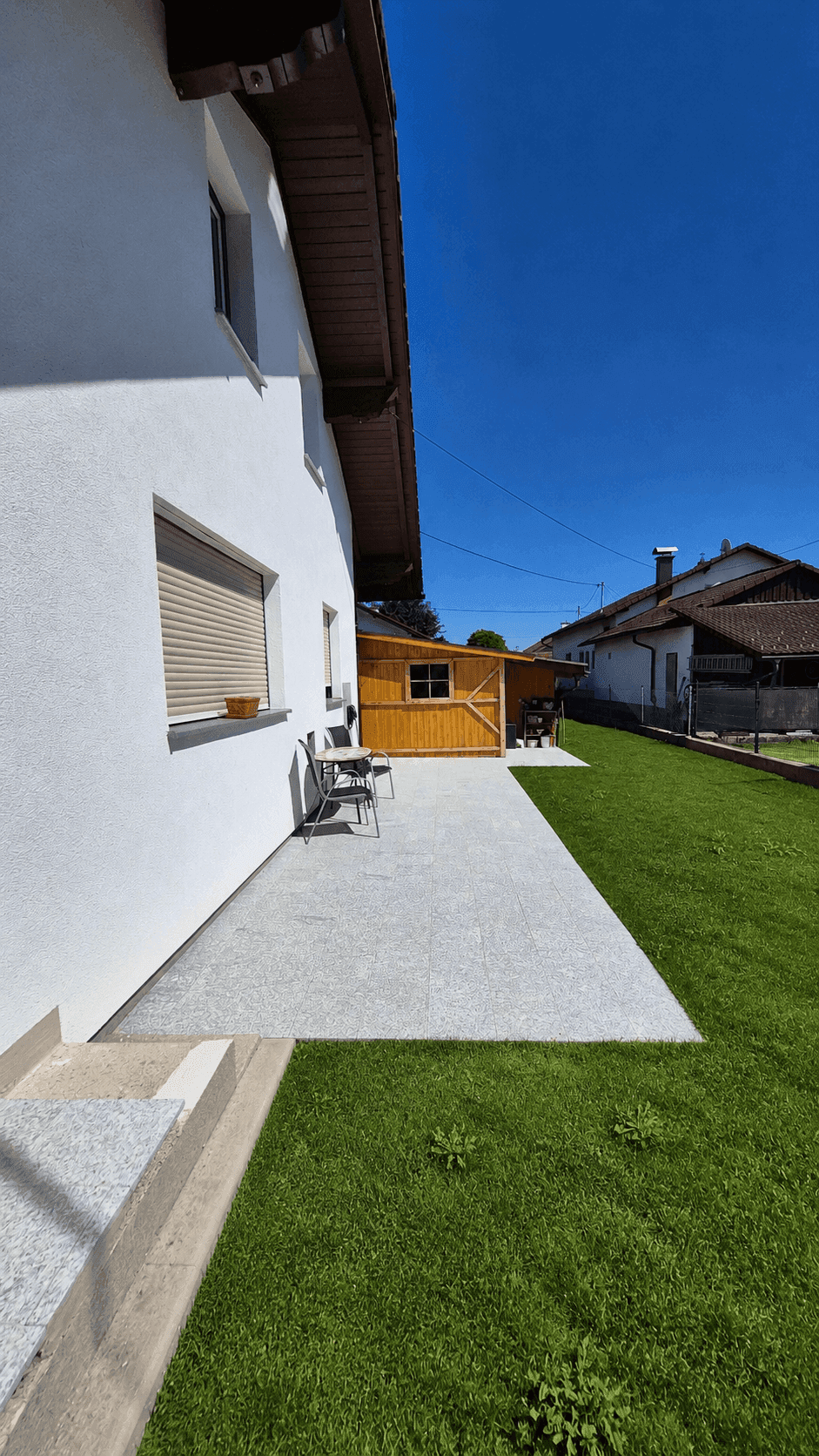 Gartenbereich mit Rasenfläche und gepflastertem Weg entlang der Hausfassade.