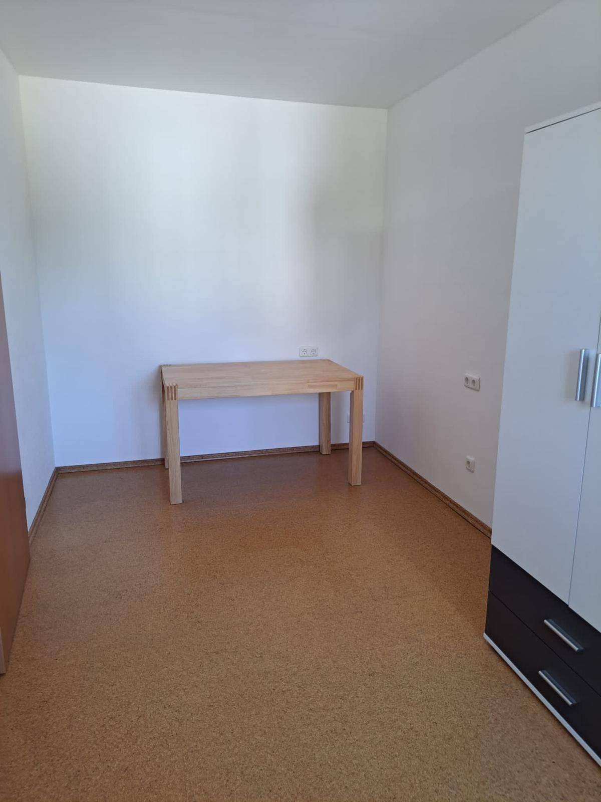 Kleines Zimmer mit Korkboden und Holztisch, nutzbar als Büro oder Gästezimmer.