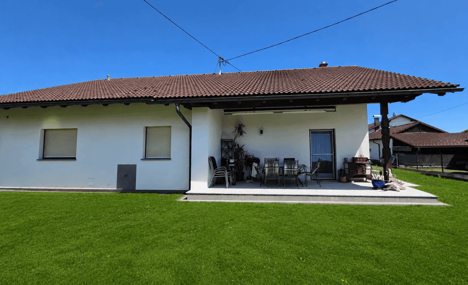 Rückseite des Hauses mit überdachter Terrasse, Garten und Sitzgelegenheiten im Freien.