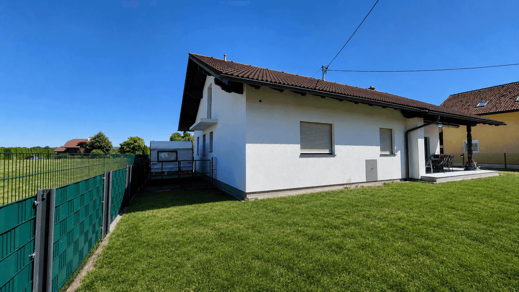 Seitenansicht des Hauses mit großem Rasenbereich und Blick auf die umliegende Landschaft.