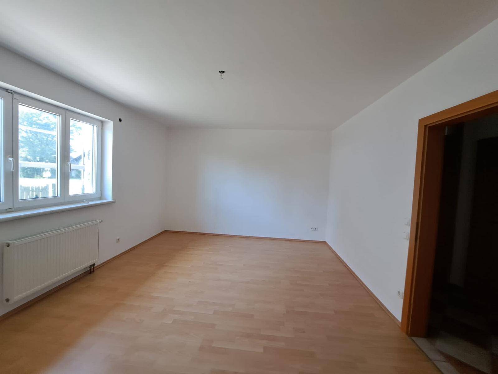 Geräumiges Wohnzimmer mit Laminatboden und viel Tageslicht durch große Fenster.