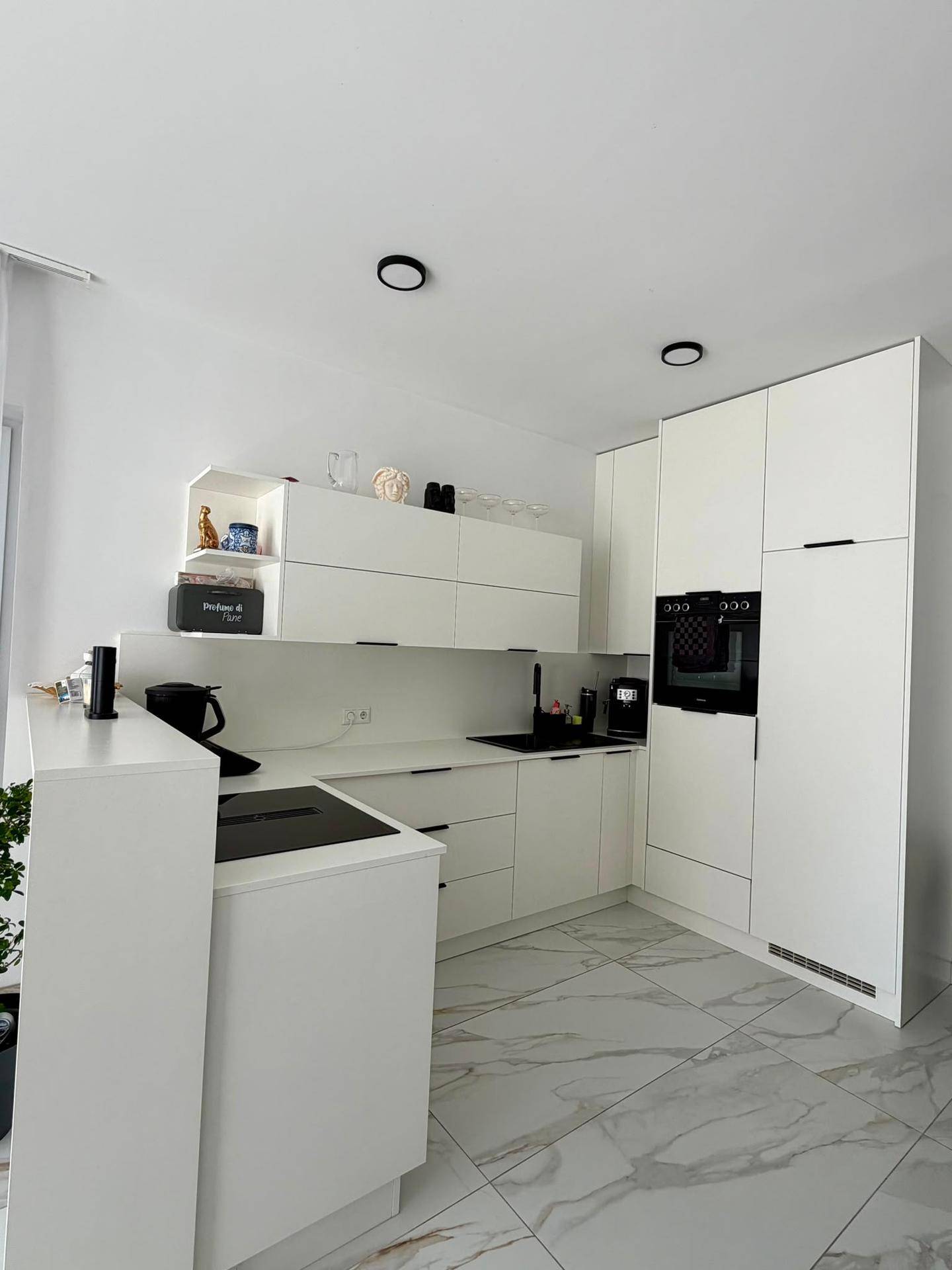 Moderne weiße Einbauküche mit integrierten Geräten und elegantem Fliesenboden.