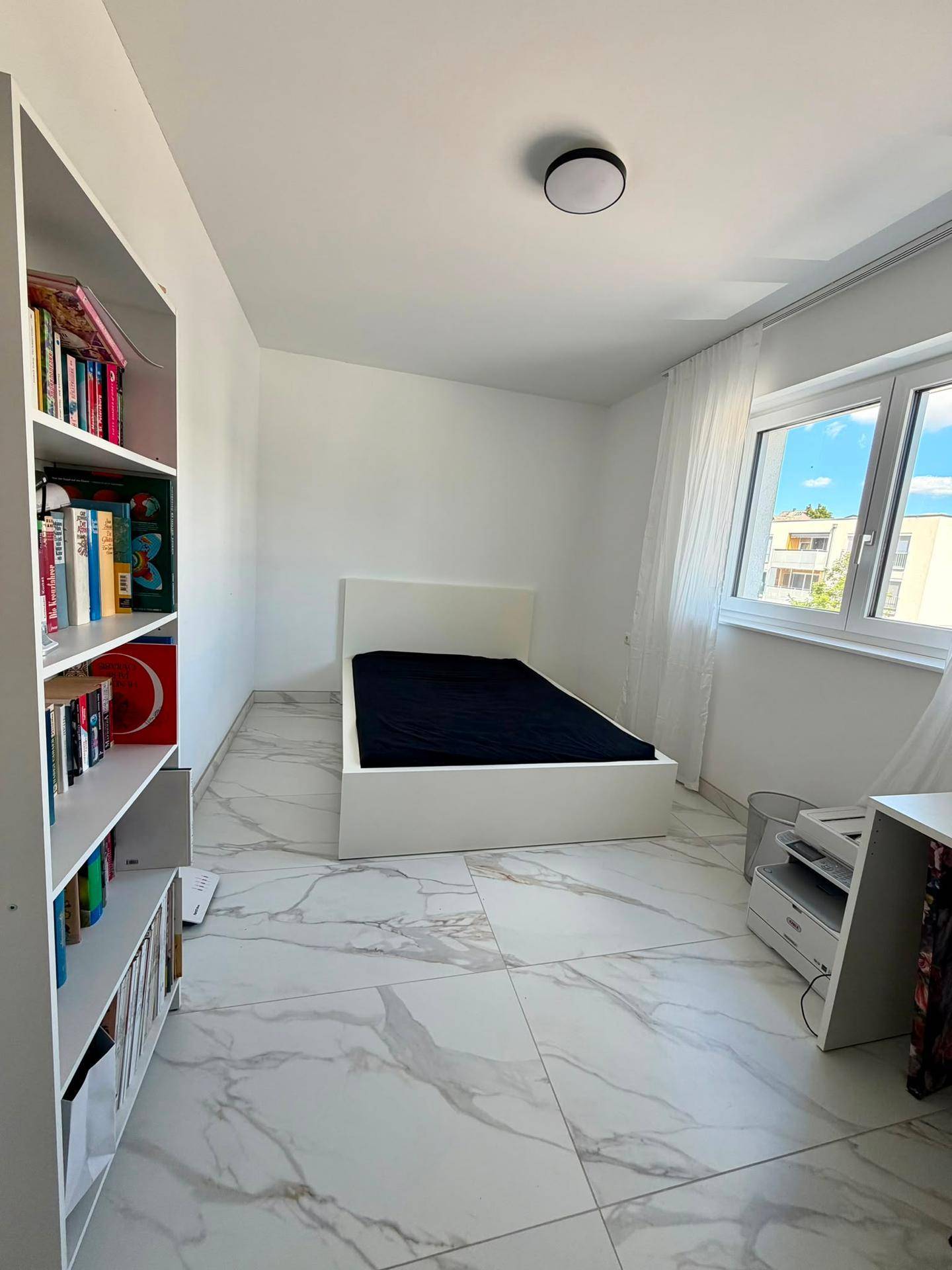Helles Zimmer mit Bett, Bücherregal und großem Fenster, ideal als Gäste- oder Kinderzimmer.