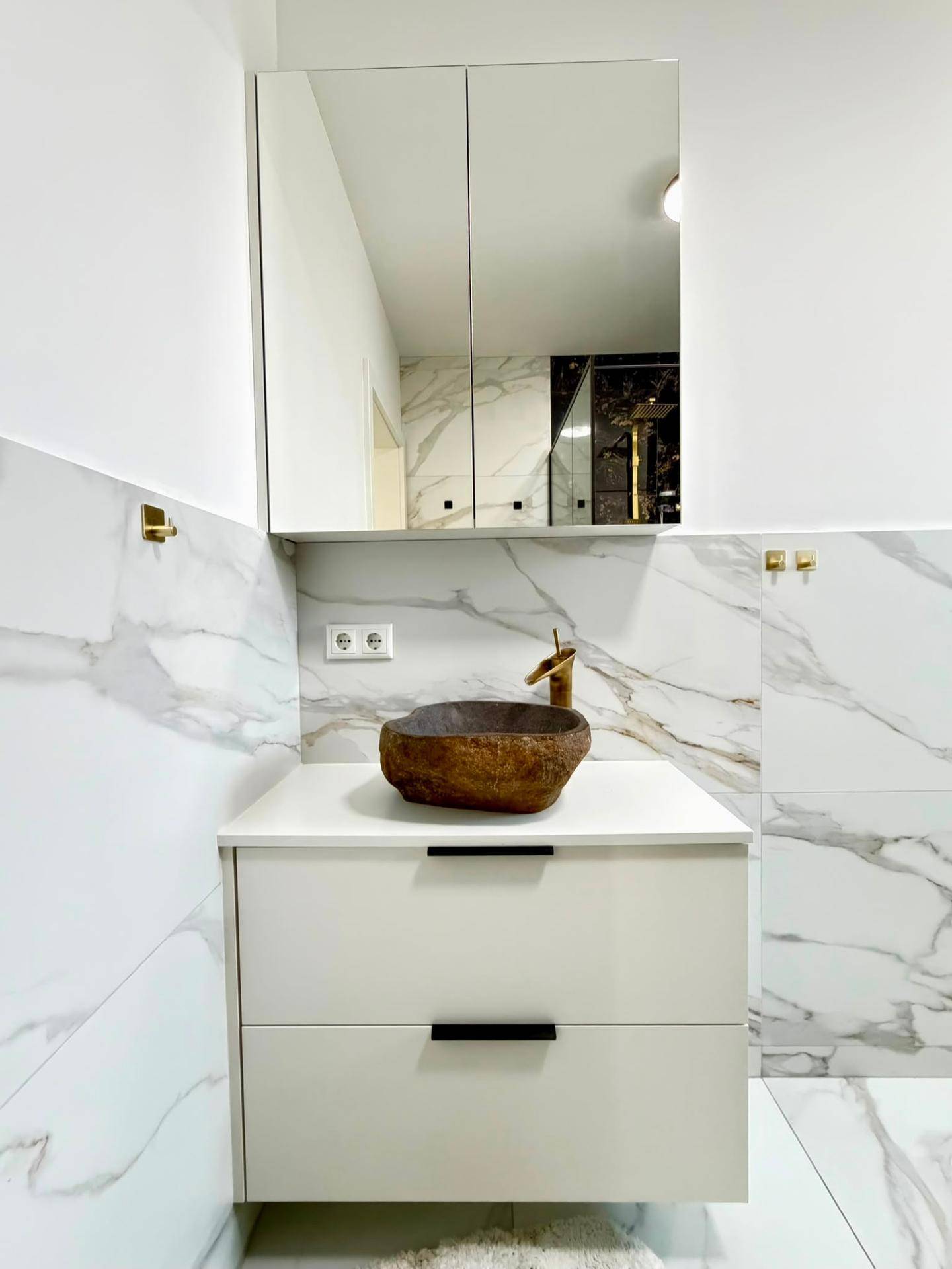 Modernes Badezimmer mit Marmorfliesen, einzigartigem Steinwaschbecken und Spiegelschrank.