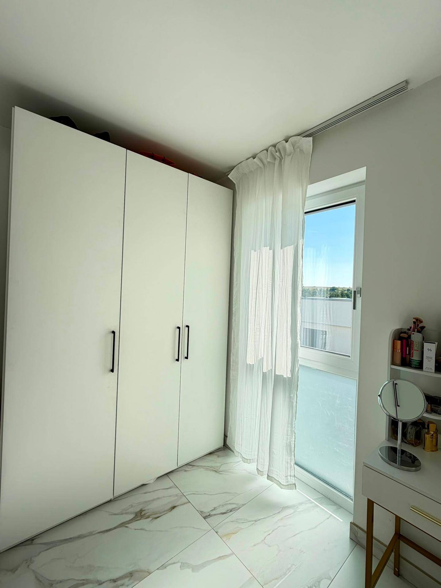 Schlafzimmer mit großen weißen Einbauschränken und Fenster für viel Tageslicht.