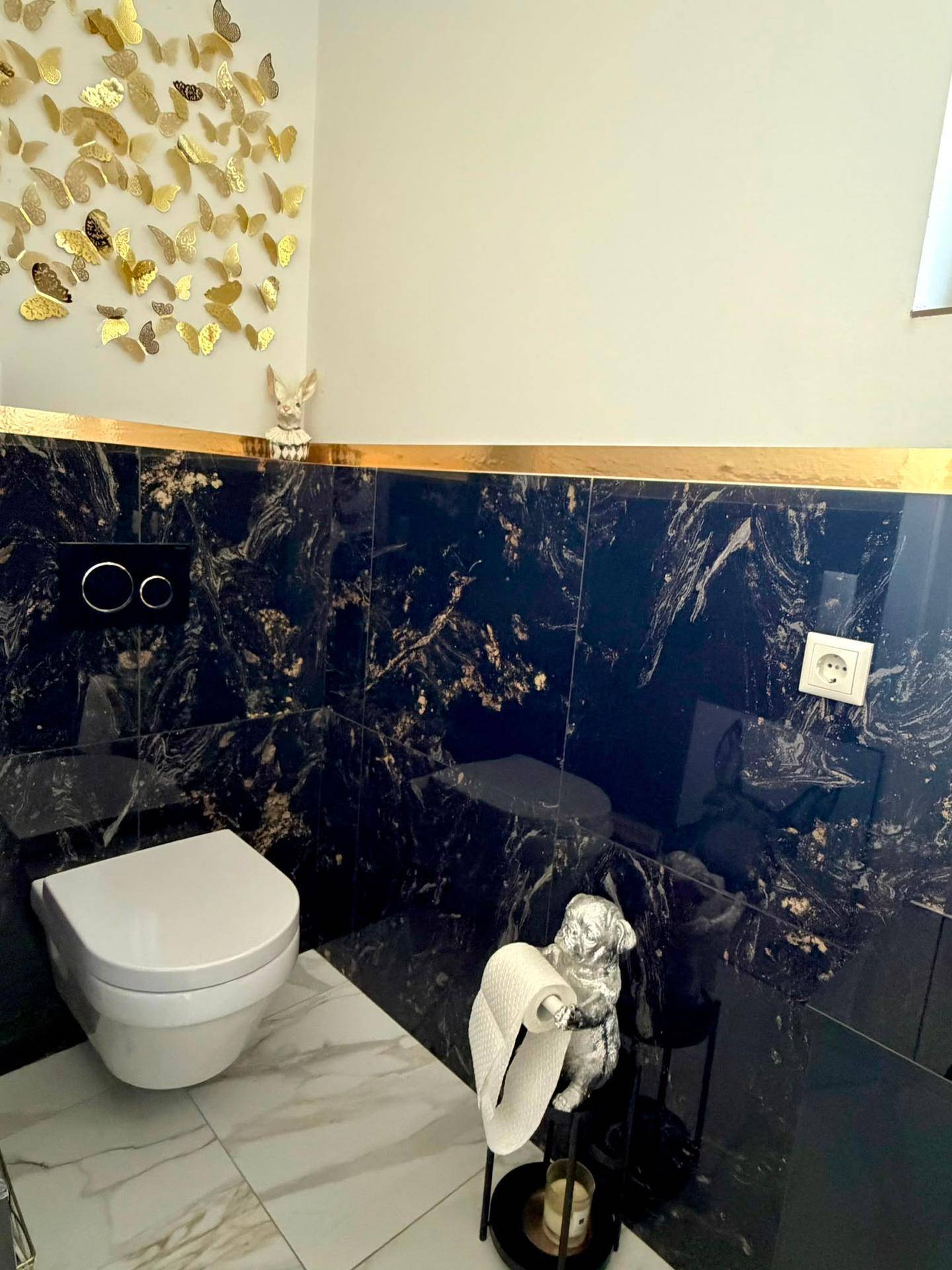 Elegantes Gäste-WC mit dunklen Marmorfliesen, Wand-WC und goldener Dekoration.