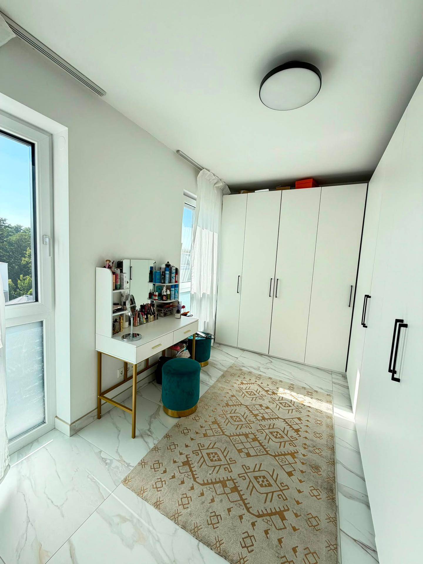 Helles Schlafzimmer mit Einbauschränken, Schminktisch und Zugang zum Balkon.