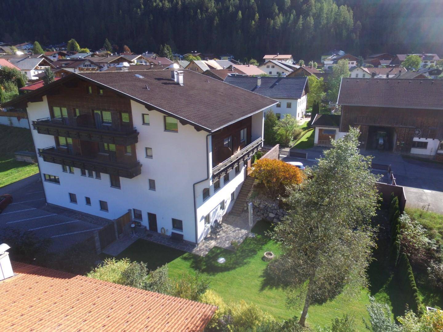 Mehrstöckiges Gebäude mit Holzbalkonen und gepflegtem Garten in alpiner Umgebung.