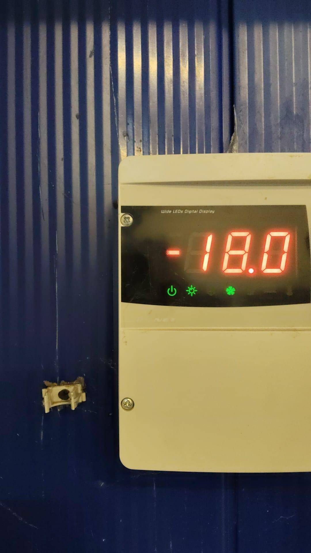 Digitalanzeige an einer blauen Wand, die eine Temperatur von -18,0 Grad Celsius anzeigt, wahrscheinlich in einem Kühlraum.