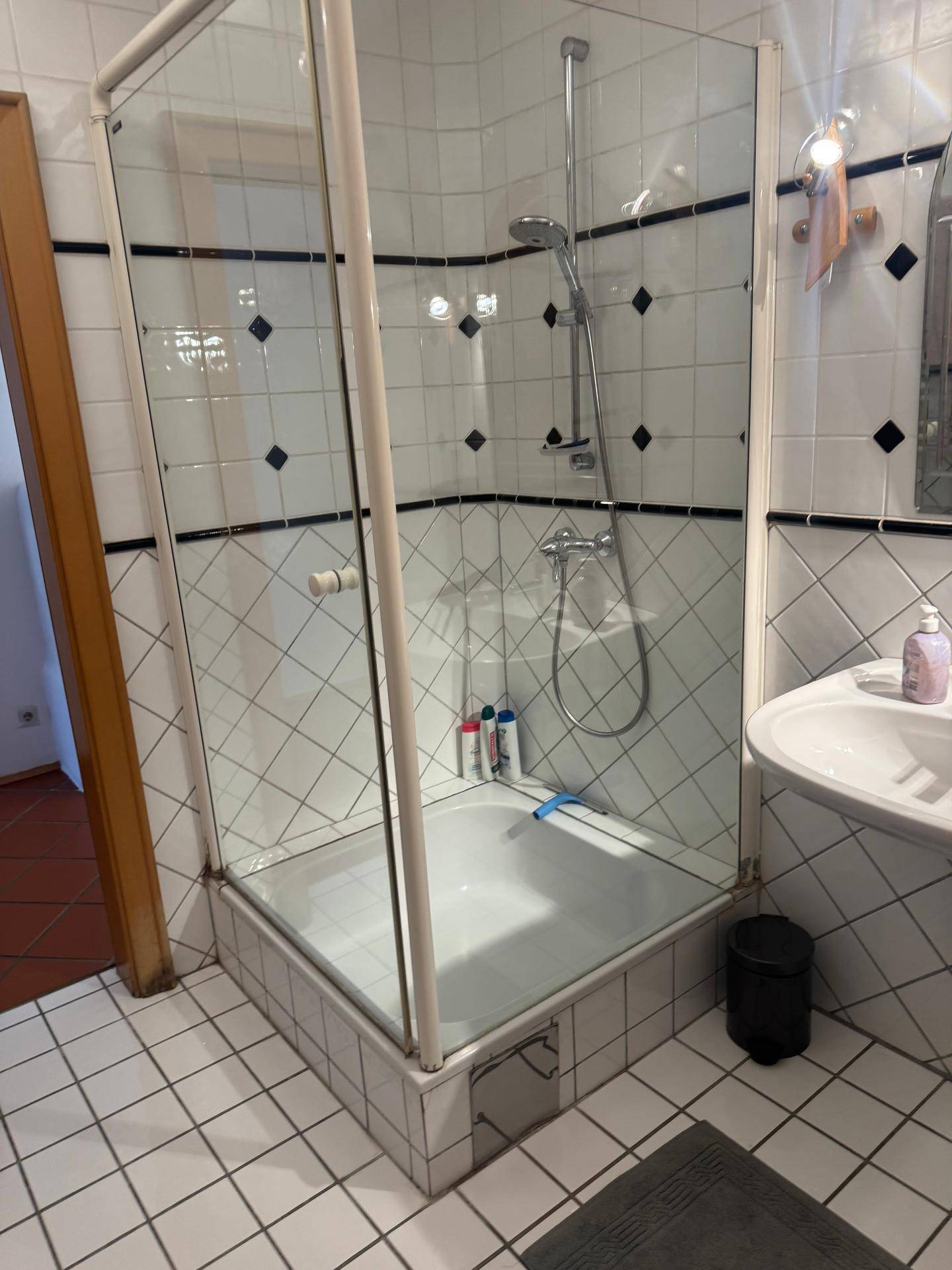 Duschbereich im Badezimmer mit weißen Fliesen, schwarzem Dekor und einer Glasduschkabine.