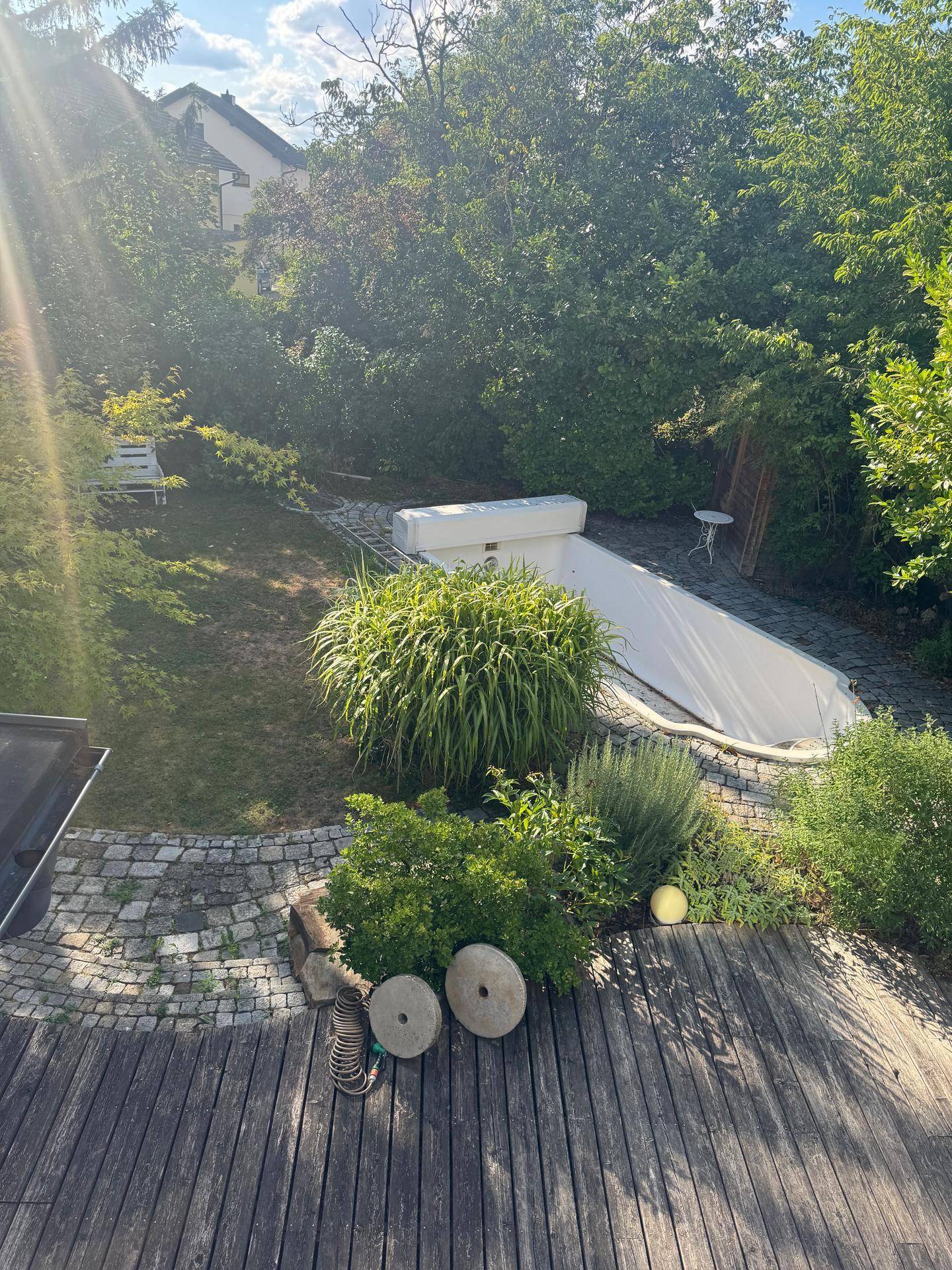 Blick von einer Holzterrasse auf den Garten mit Pool und üppiger Vegetation.