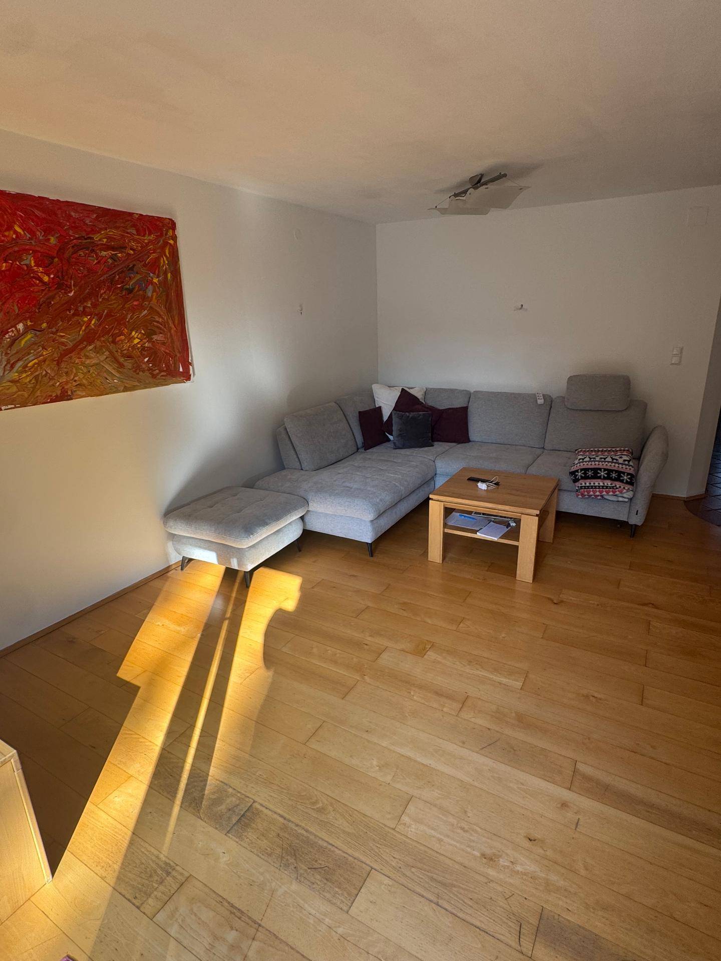 Gemütliches Wohnzimmer mit großem Ecksofa, Holzboden und einem farbenfrohen Kunstwerk an der Wand.