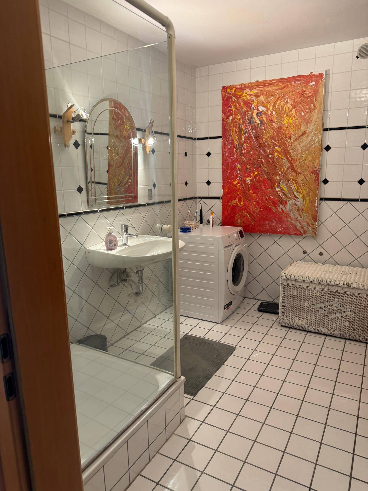 Badezimmer mit weiß-schwarzen Fliesen, Waschbecken, Waschmaschine und einer Duschkabine.