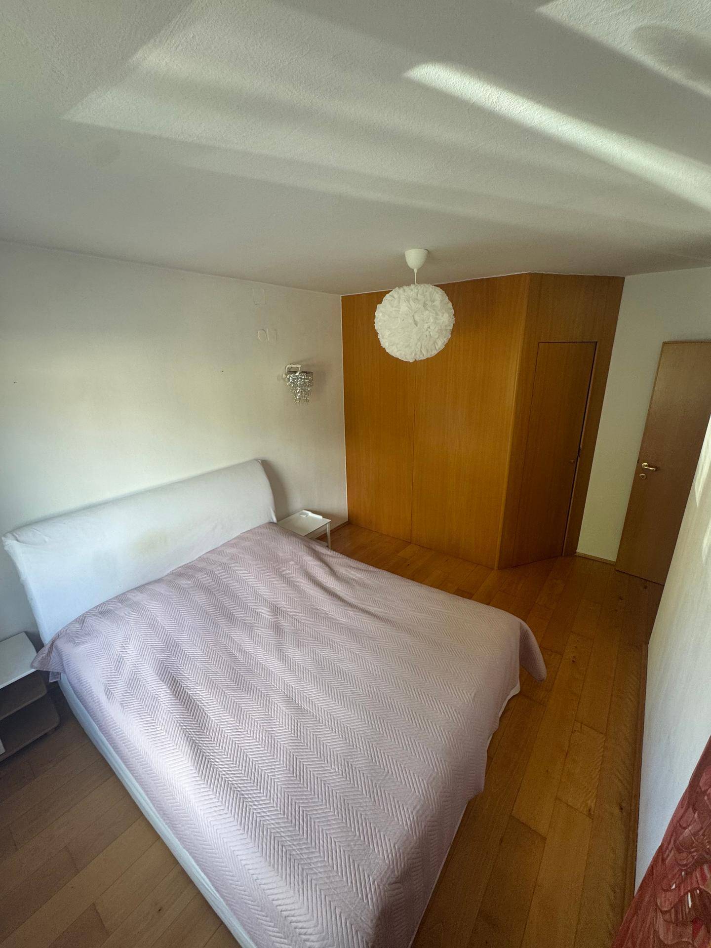 Schlafzimmer mit weißem Bett, Holzwandverkleidung und hellem Parkettboden.