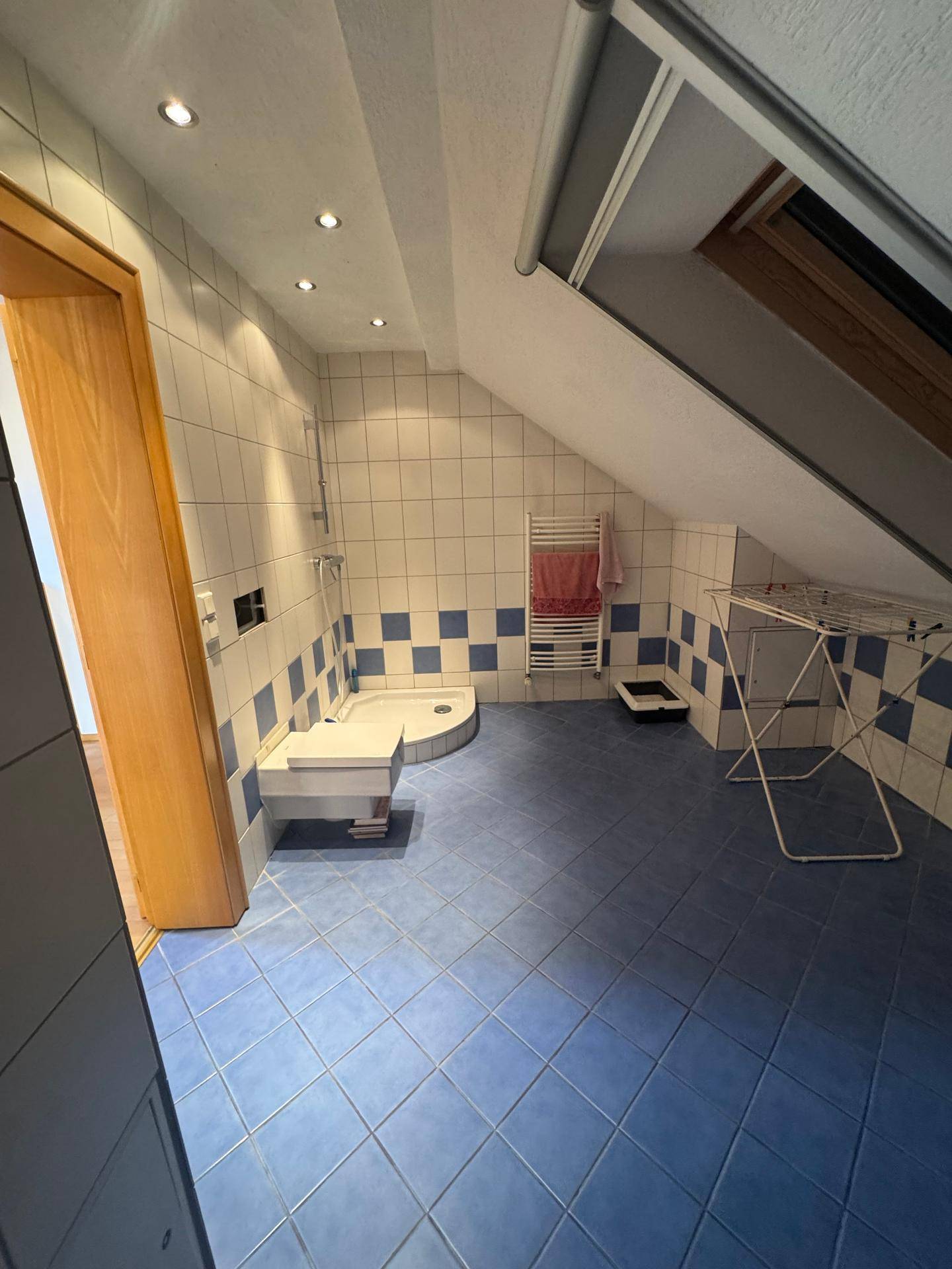 Dachgeschoss-Badezimmer mit blau-weißen Fliesen, Dusche, beheiztem Handtuchhalter und Dachfenster.