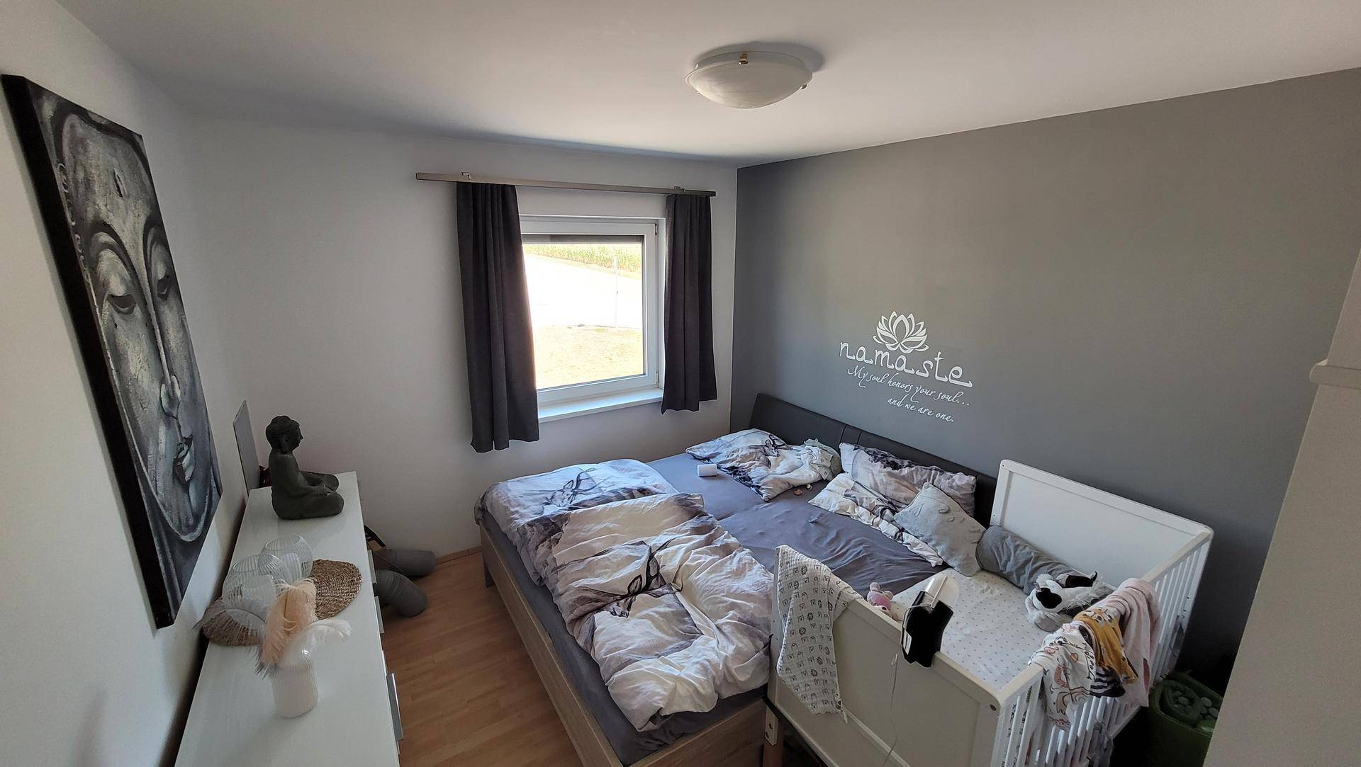 Gemütliches Schlafzimmer mit Doppelbett, Babybett und Fenster, dekoriert mit Wandkunst.