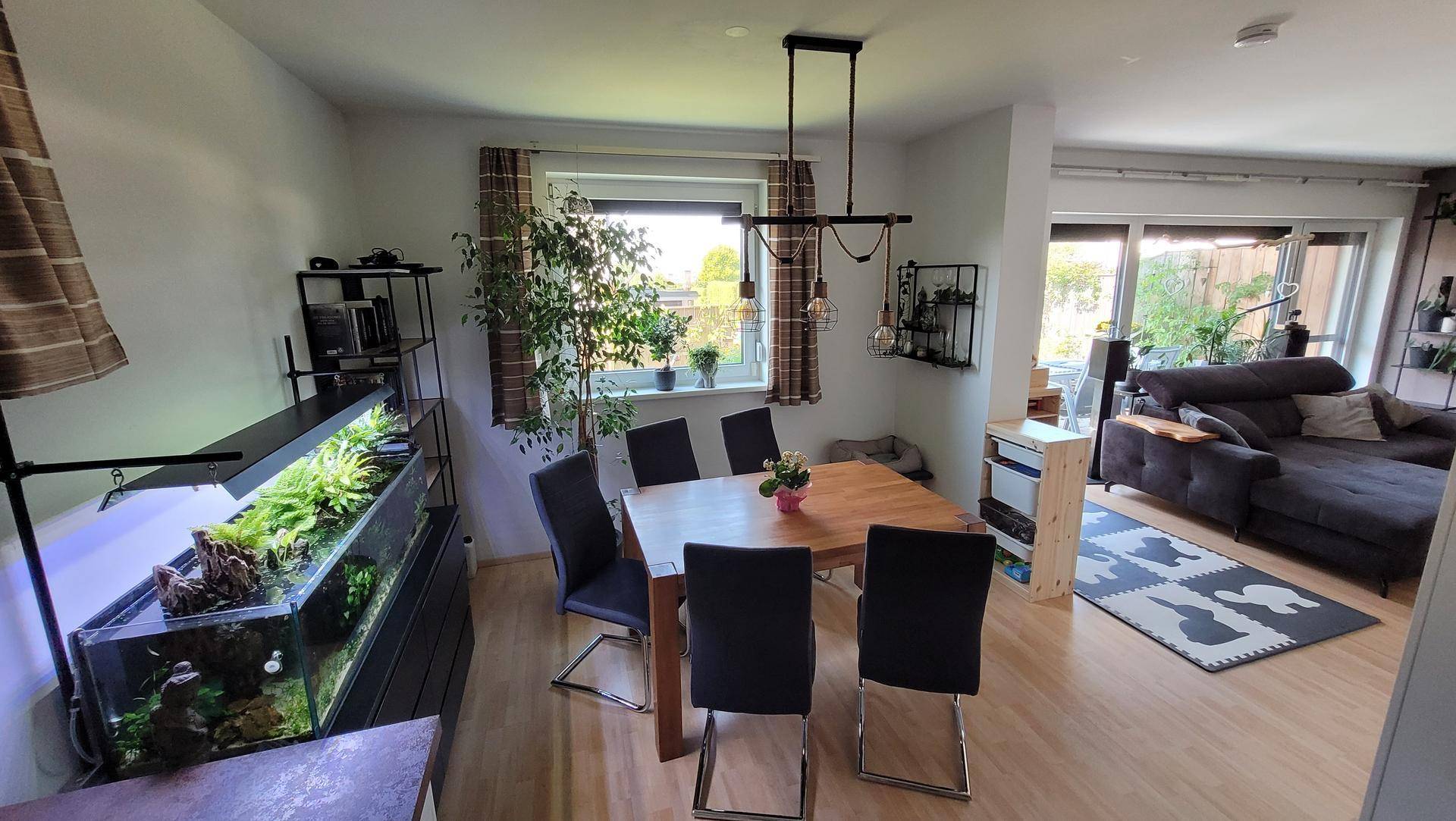Heller Essbereich mit Holztisch und Stühlen, offen zum Wohnzimmer, mit großem Aquarium und Pflanzen.