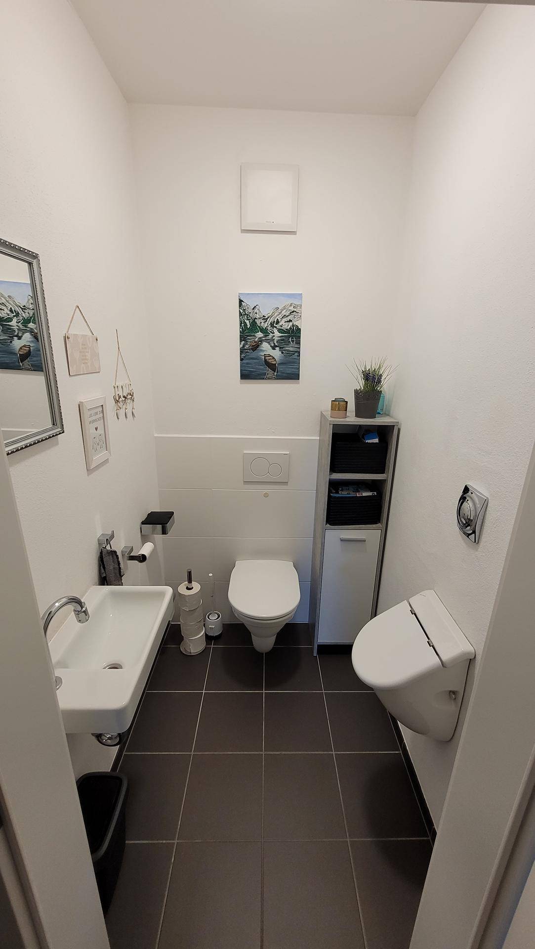 Separates Gäste-WC mit Wand-WC, Urinal und kleinem Waschbecken, sauber und hell.