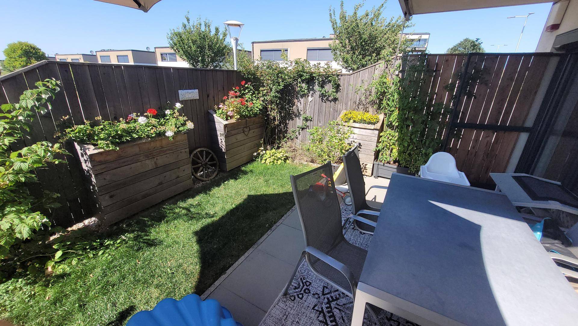 Gemütlicher Gartenbereich mit Holzumzäunung, bepflanzten Hochbeeten und einer Terrasse mit Sitzgelegenheiten.