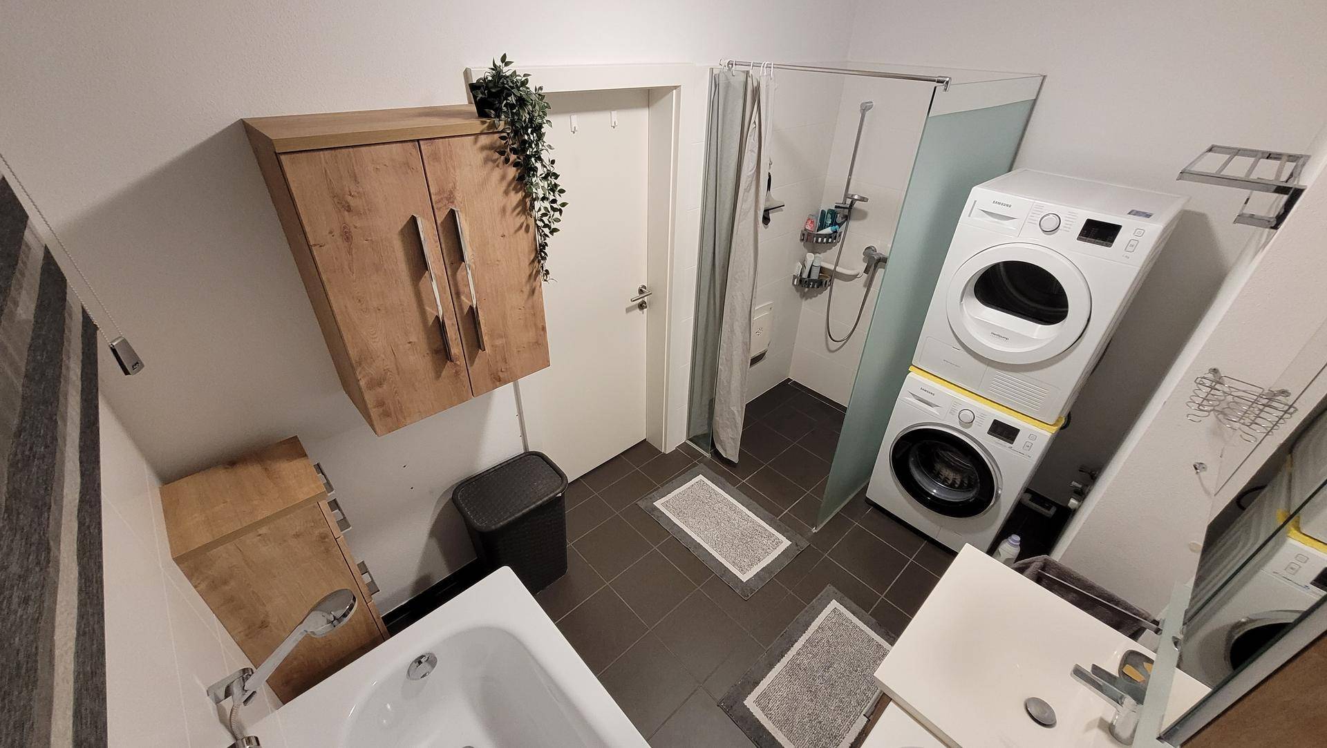 Modernes Badezimmer mit Dusche, Badewanne, Waschmaschine und Trockner, funktional eingerichtet.