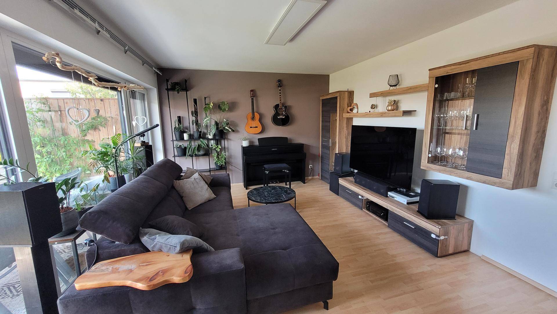 Modernes Wohnzimmer mit großem Ecksofa, Holzboden und Zugang zu einem hellen Außenbereich.