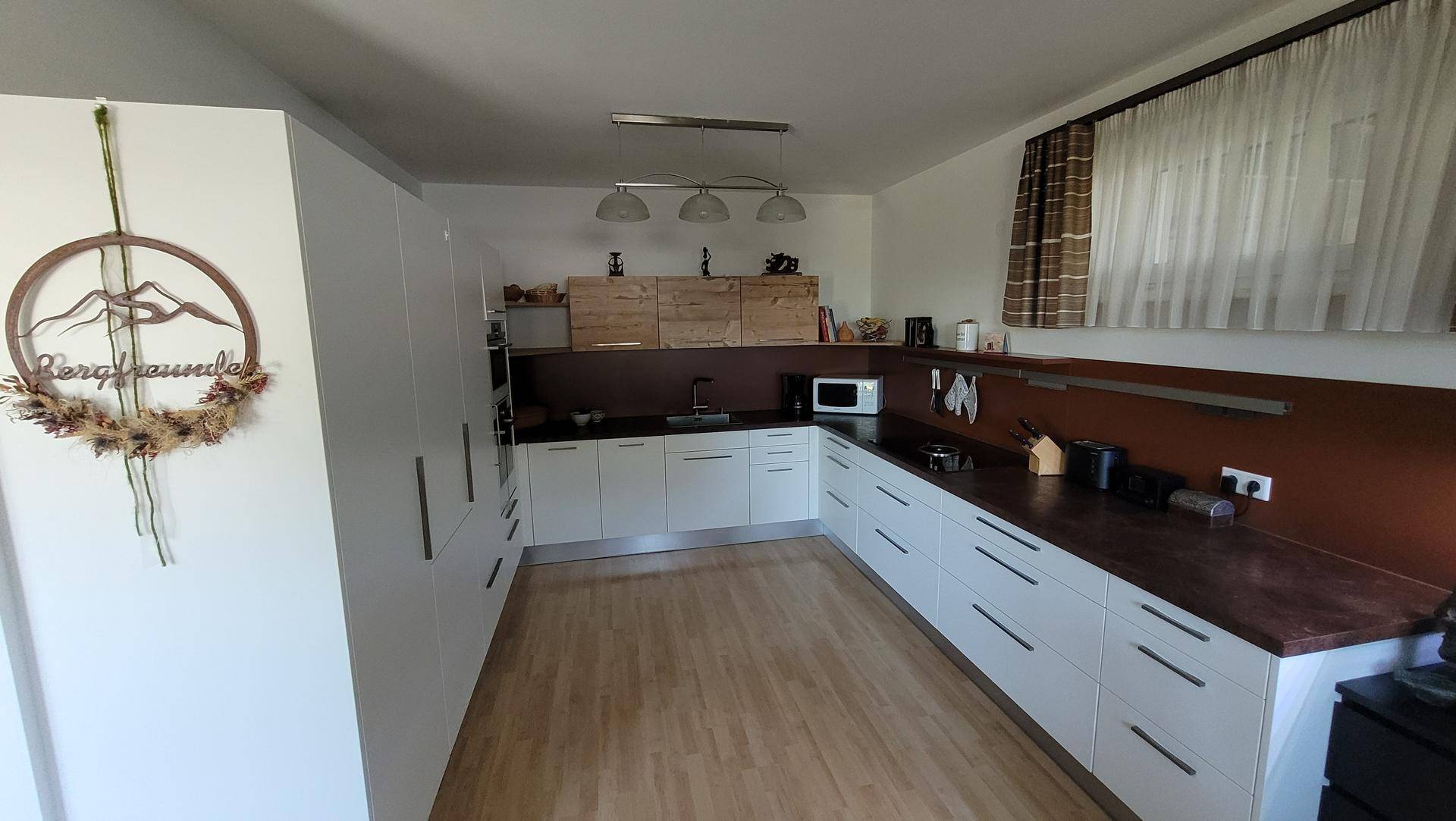 Moderne Einbauküche mit weißen Fronten, dunkler Arbeitsplatte und Holzdetails, gut beleuchtet.