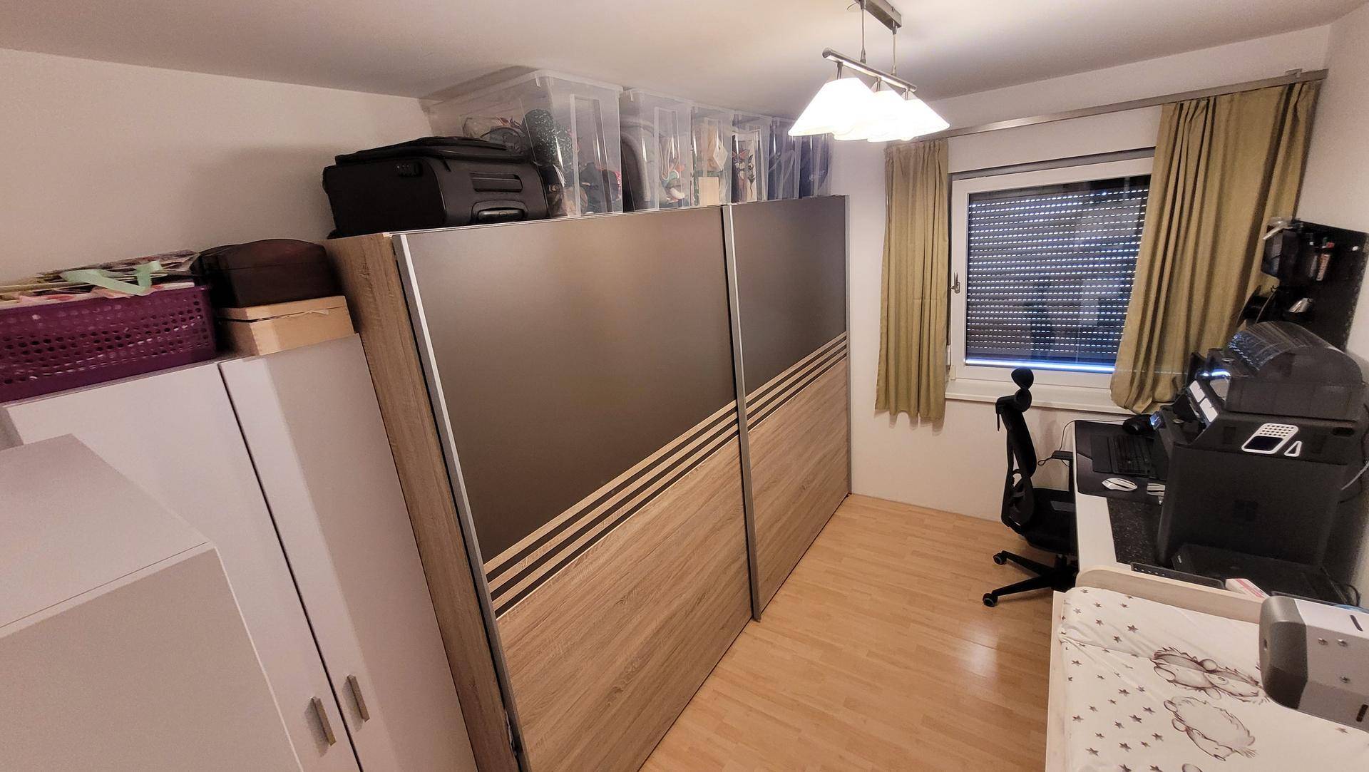 Schlafzimmer oder Arbeitszimmer mit Schiebetürenschrank, Holzboden und Fenster mit Rollladen.