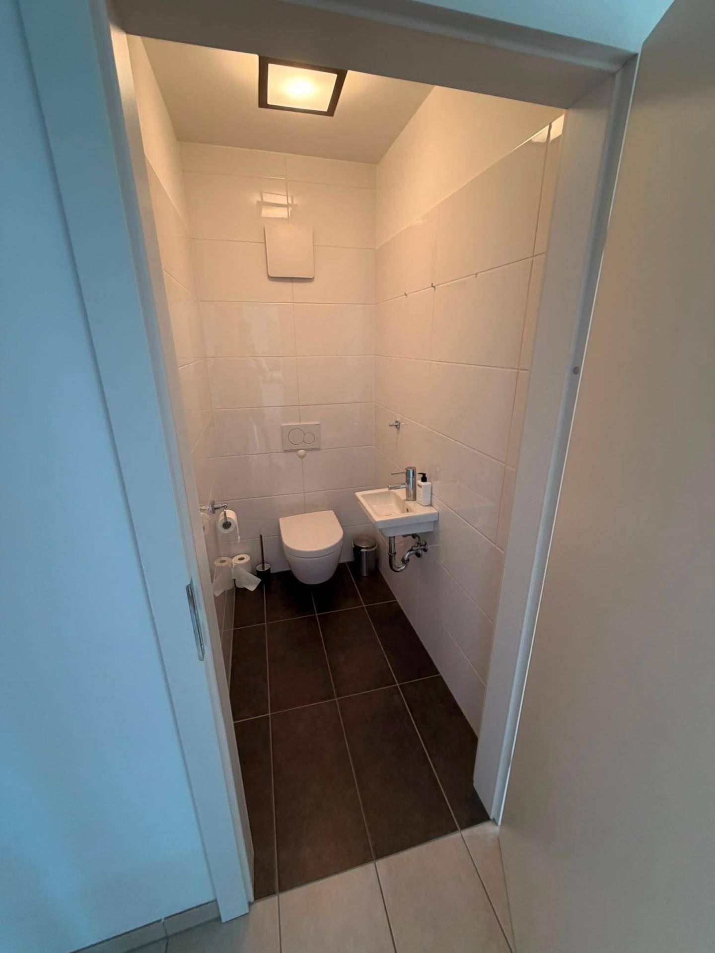 Kleines Gäste-WC mit weißen Wandfliesen, dunklem Boden und wandhängendem WC.