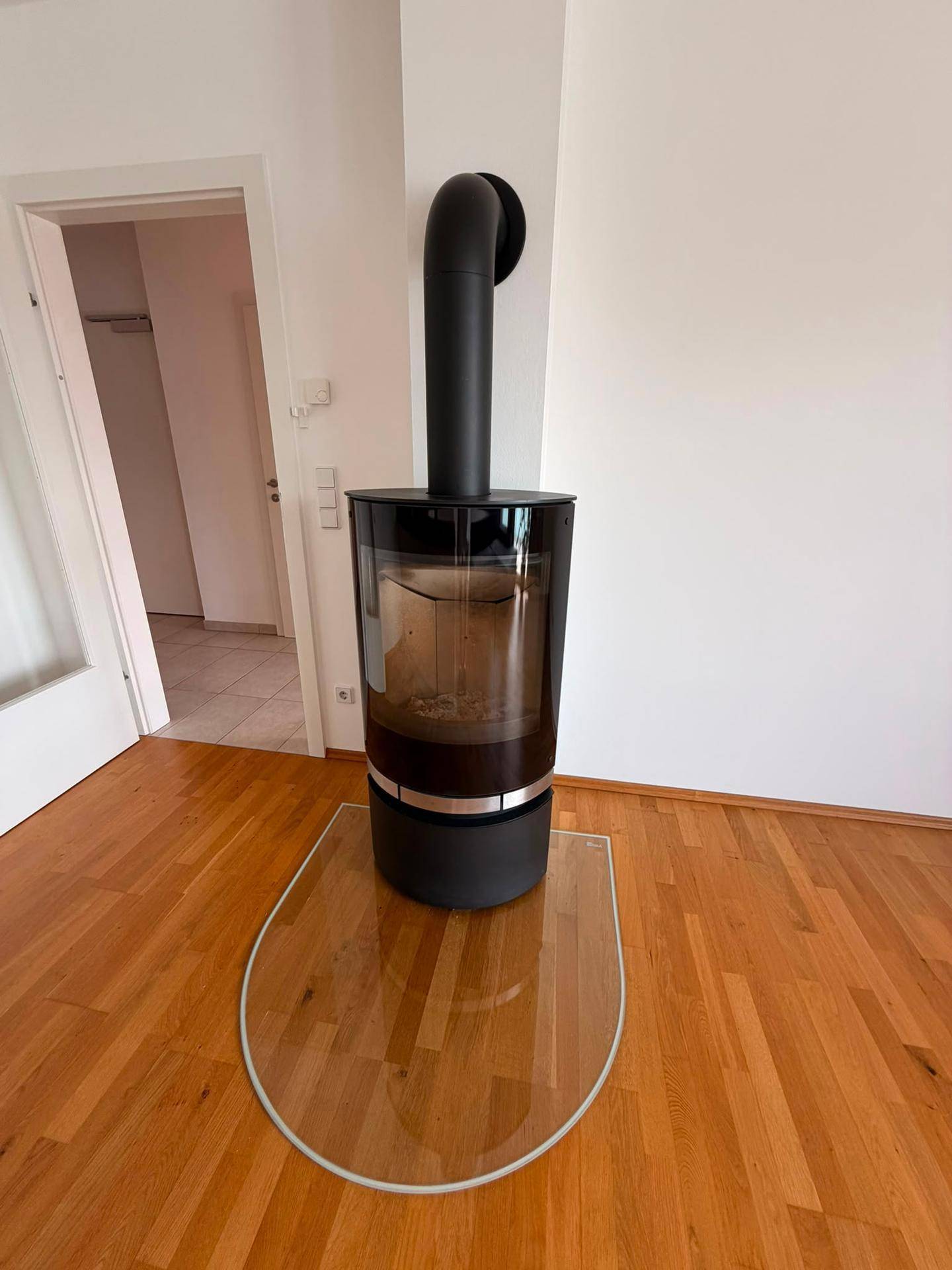 Moderner Holzofen mit Glasfront auf einem Schutzboden aus Glas im Wohnbereich.