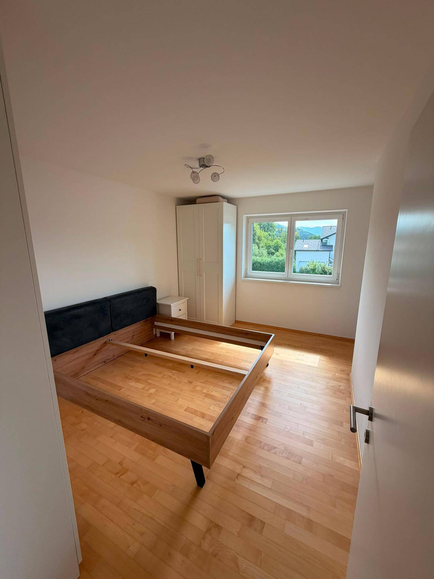 Schlafzimmer mit Holzboden, Bettrahmen und weißem Kleiderschrank, hell und freundlich.