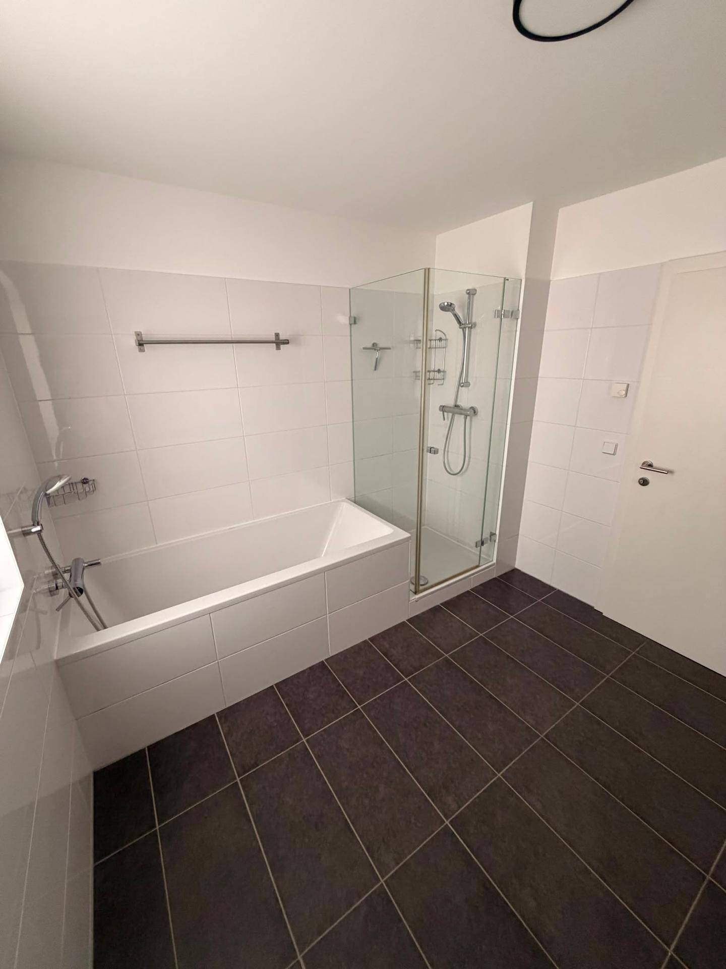 Badezimmer mit Badewanne und separater Duschkabine aus Glas, hell gefliest.