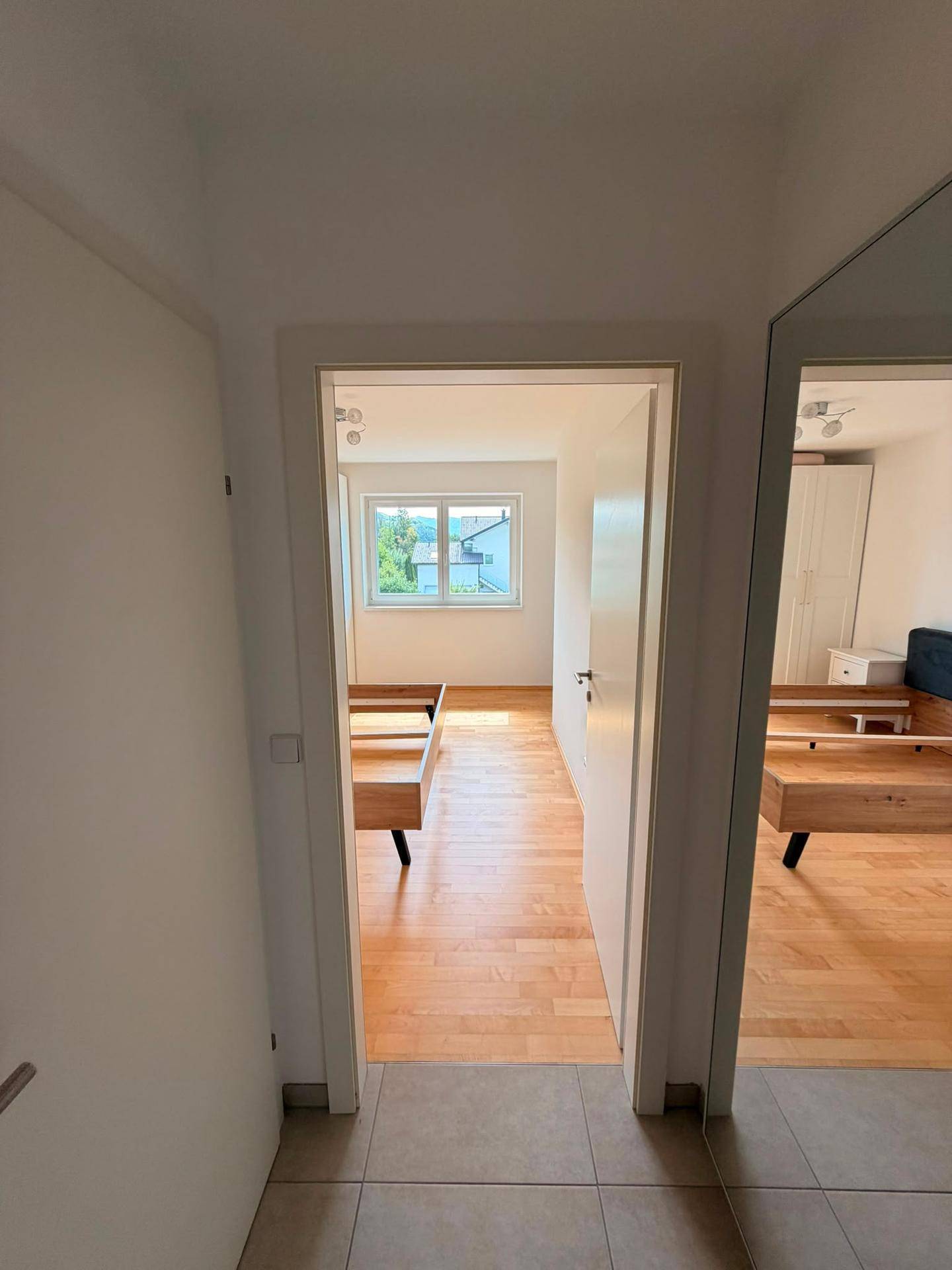 Blick vom Flur in ein Schlafzimmer mit Holzboden und Fenster, das viel Licht hereinlässt.