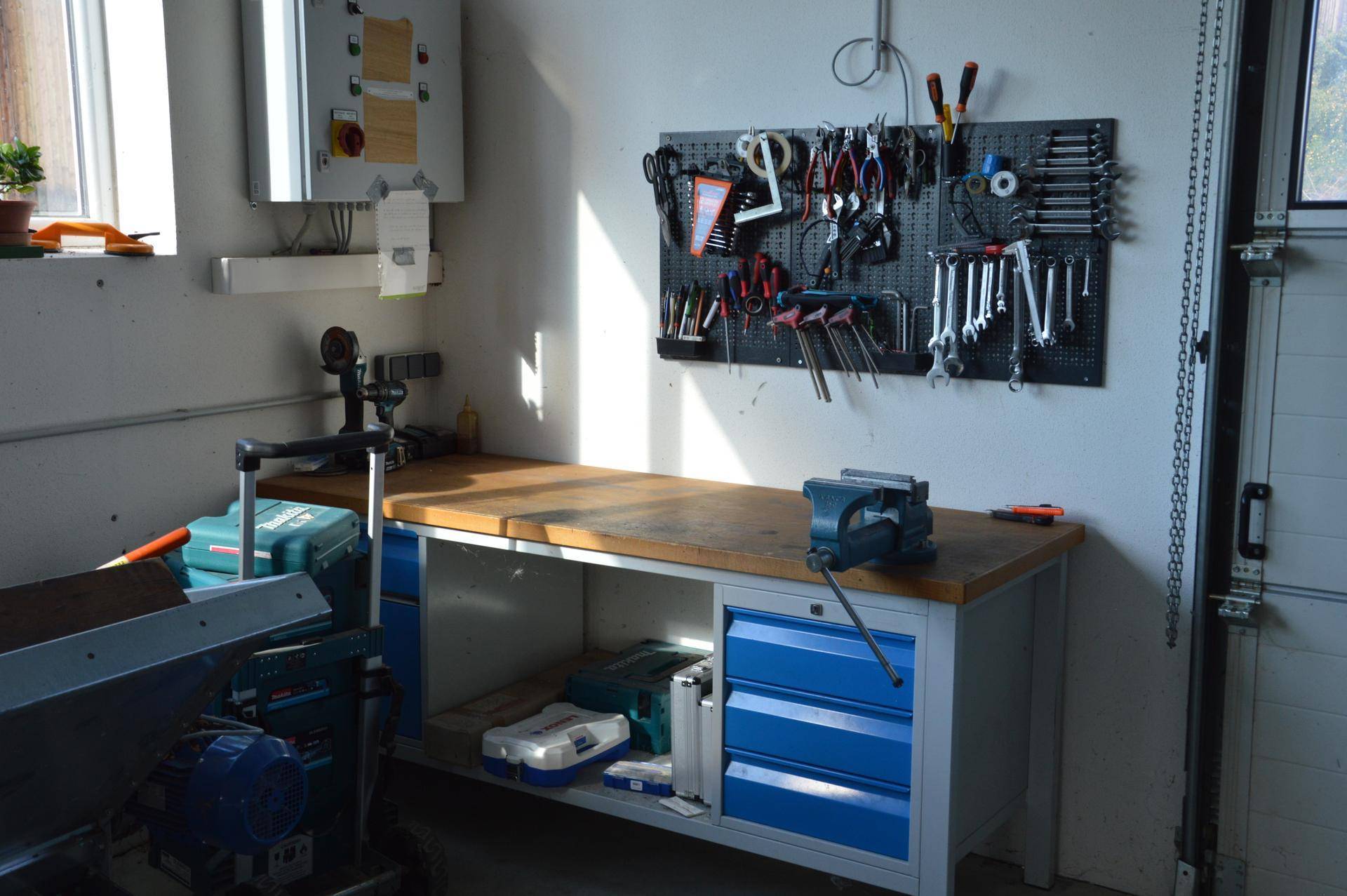 Gut ausgestattete Werkbank mit Schraubstock, Werkzeugwand und blauen Schubladen, ideal für handwerkliche Arbeiten.