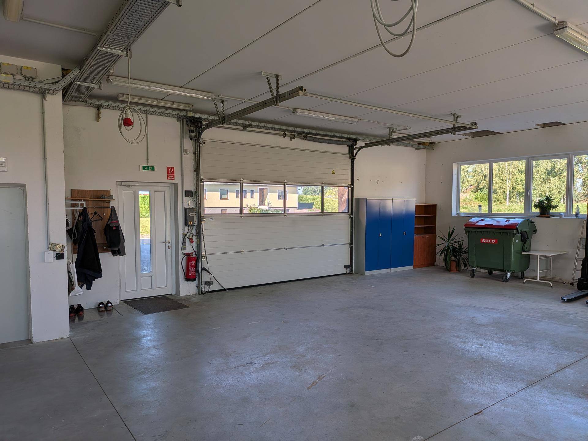 Geräumige Garage mit großem Rolltor, Betonboden und Fenstern, bietet viel Platz für Fahrzeuge oder Lagerung.
