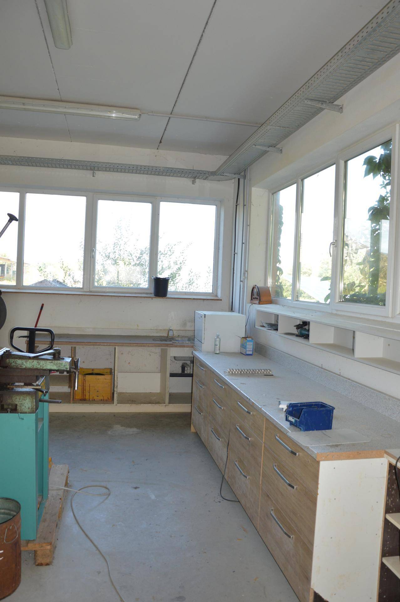 Werkstattraum mit langer Arbeitsfläche, Holzschubladen und großen Fenstern, bietet viel Licht und Stauraum.