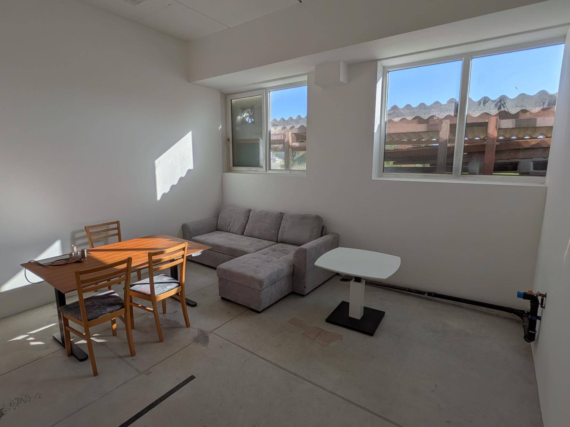 Gemütlicher Pausenraum mit Sofa, Esstisch und Fenstern, ideal für entspannte Momente.