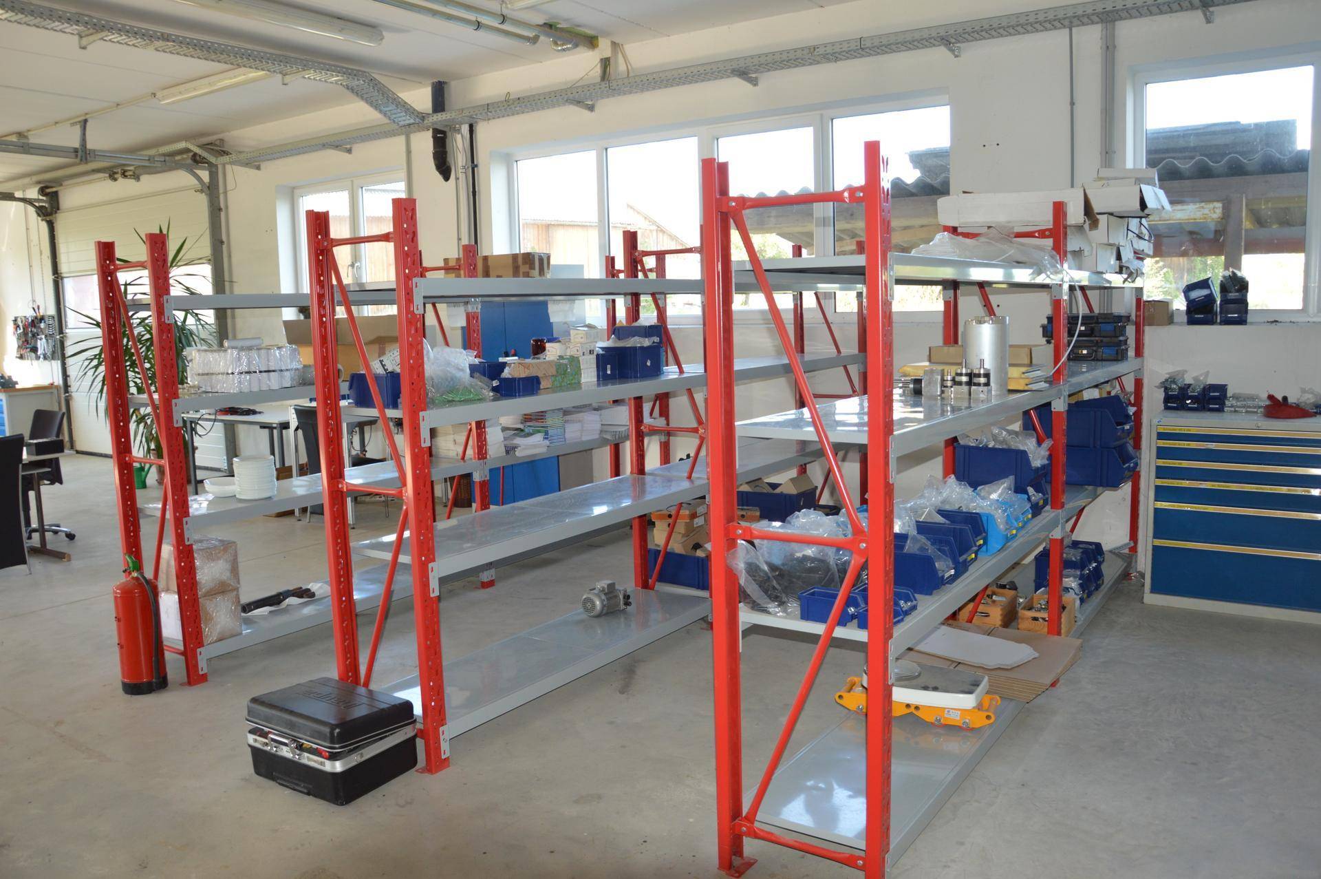 Lagerraum mit robusten roten Regalsystemen und großen Fenstern, ideal zur Organisation von Materialien.