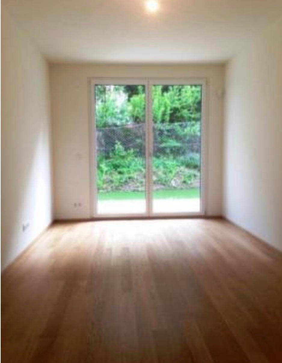 Heller Raum mit Holzboden und großem Fenster, das einen schönen Blick ins Grüne bietet.