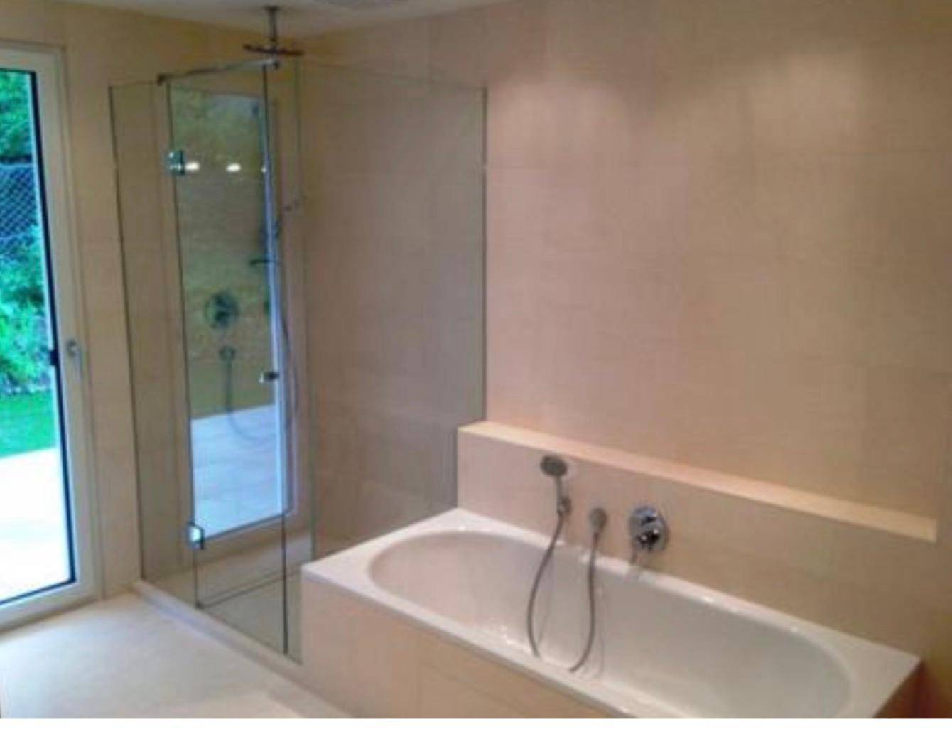 Helles Badezimmer mit Badewanne, separater Glasdusche und großem Fenster für Tageslicht.
