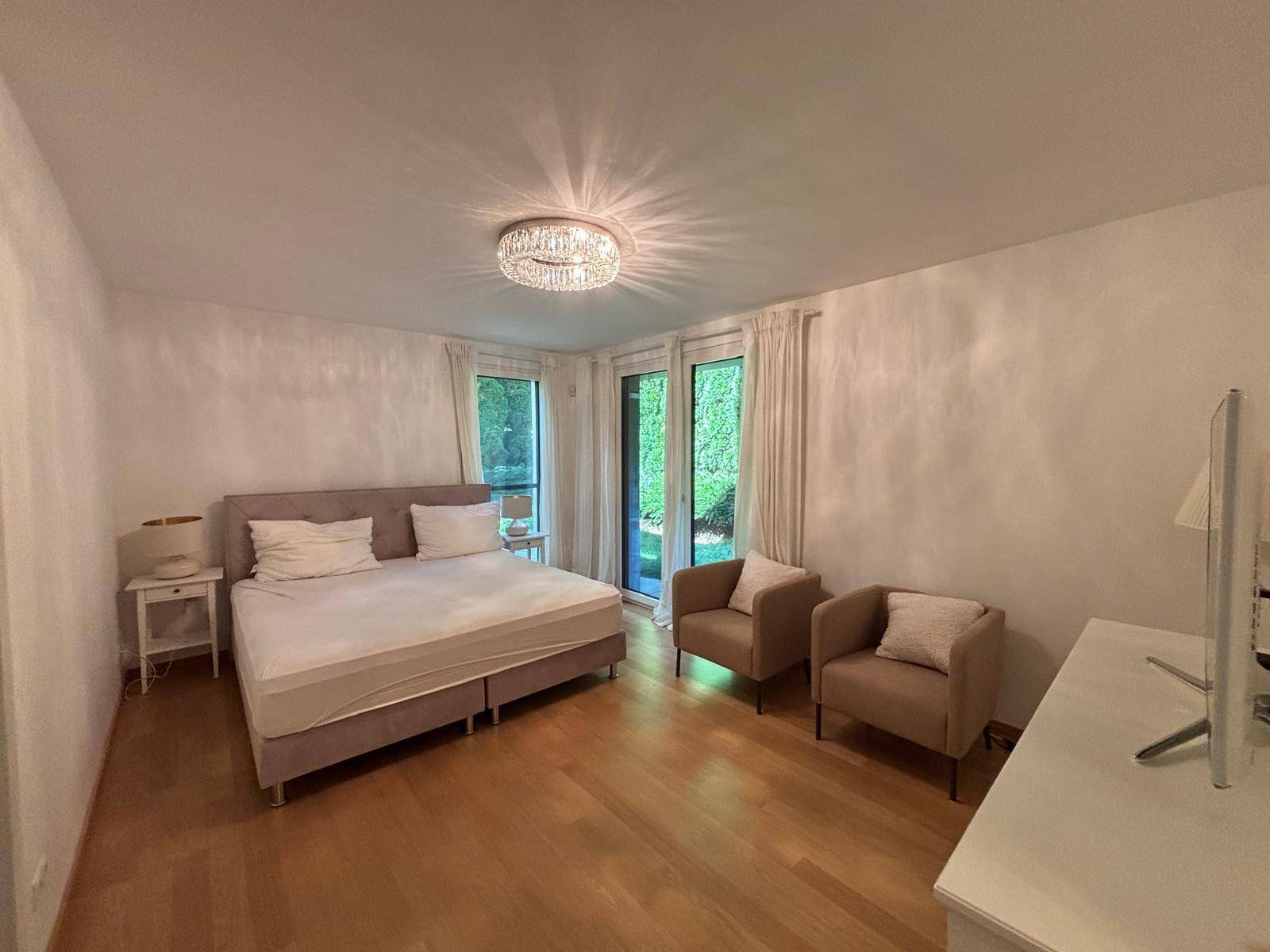 Gemütliches Schlafzimmer mit Doppelbett, zwei Sesseln und großen Fenstern mit Blick ins Grüne.