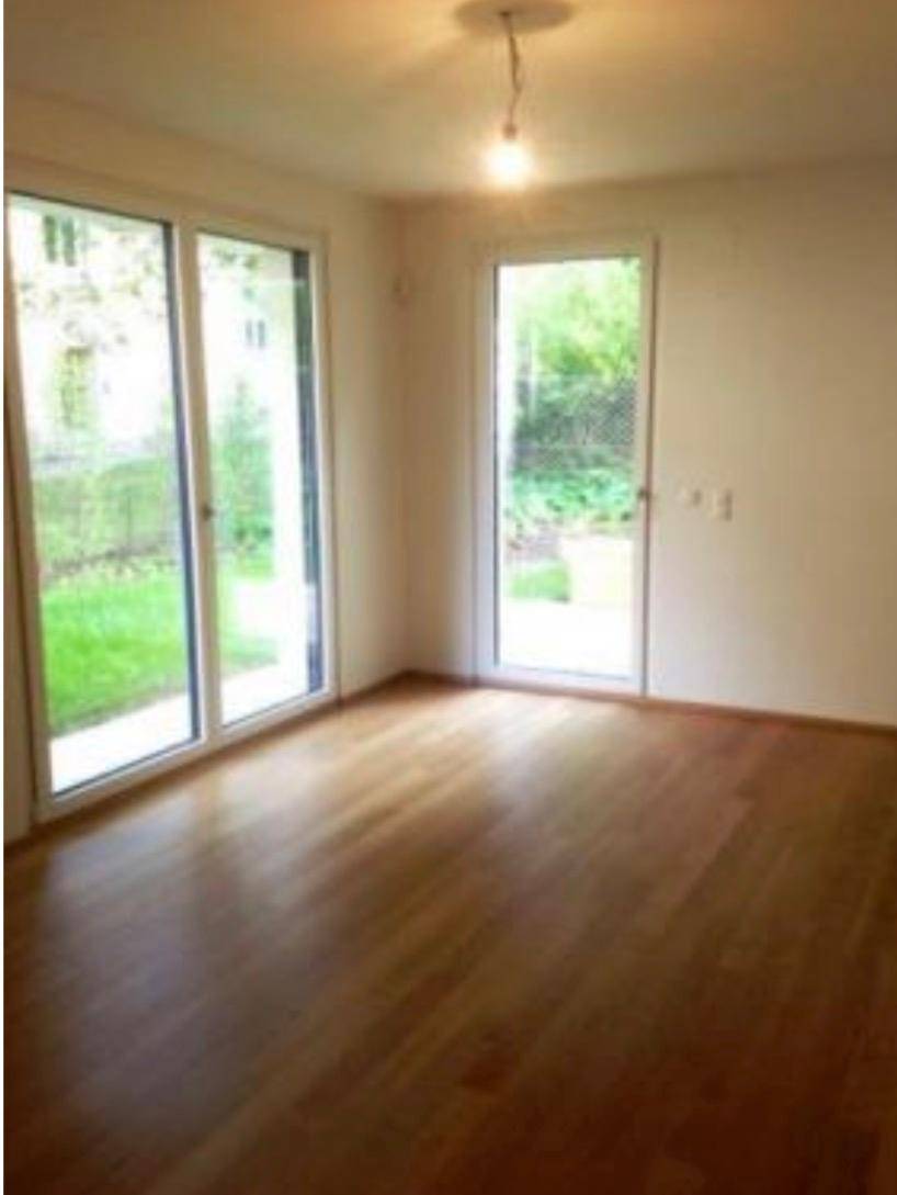 Leeres Schlafzimmer mit Holzboden und Zugang zum Garten durch große Fenstertüren.