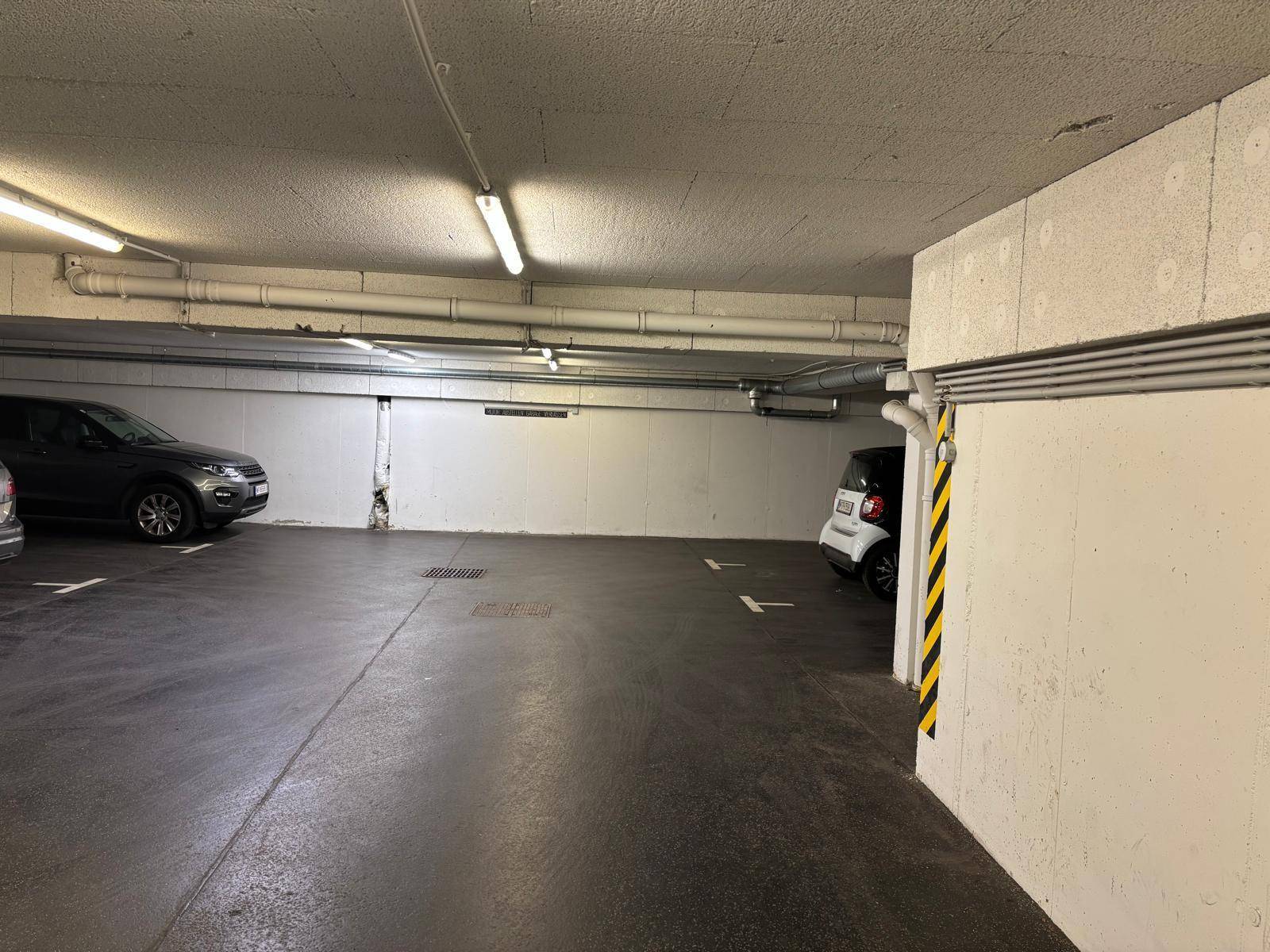Tiefgarage mit mehreren Stellplätzen und Betonwänden, gut beleuchtet.