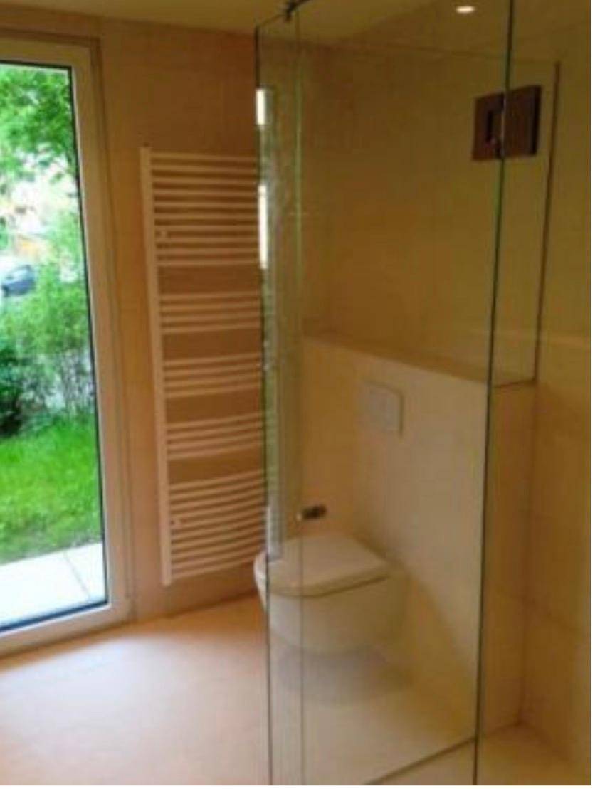 Modernes Badezimmer mit wandhängendem WC, Glasdusche, Handtuchheizkörper und Fenster.