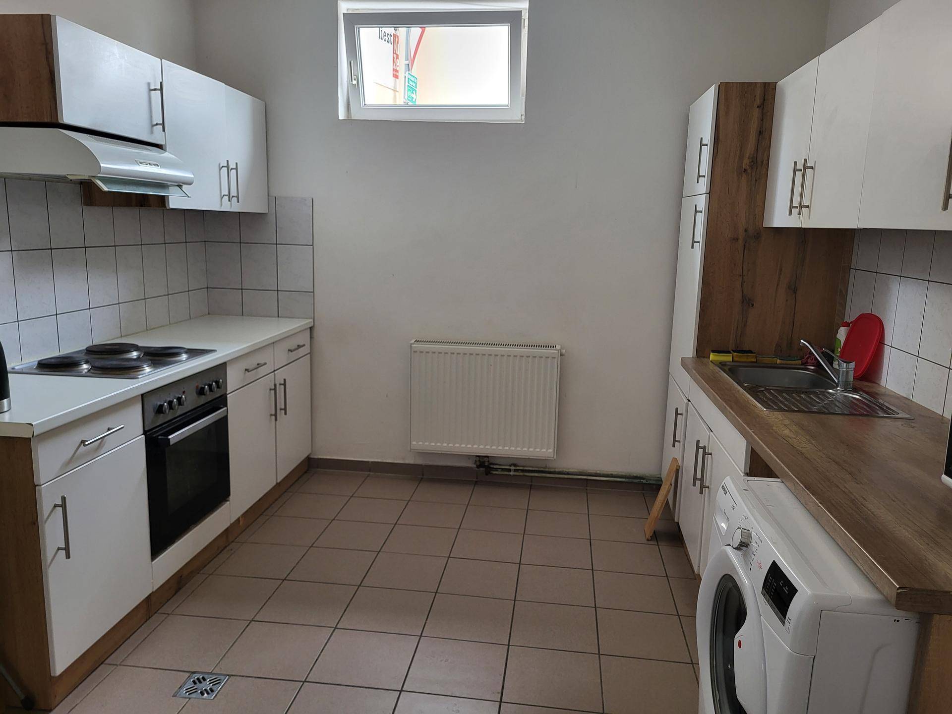 Funktionale Küche mit weißen Schränken, Holz-Arbeitsplatte, Fliesenboden und einem Fenster.