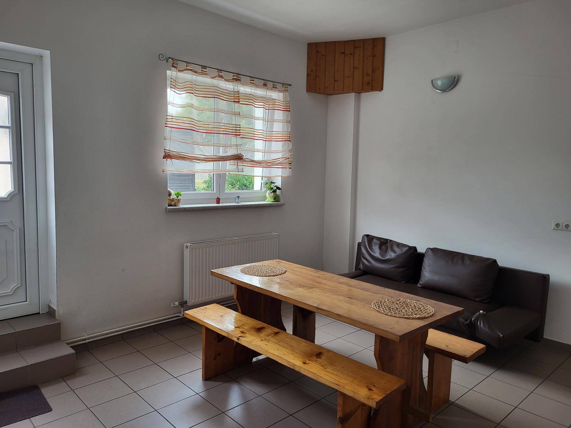 Gemütlicher Essbereich mit Holztisch, Bänken, Sofa und einem Fenster mit Blick nach draußen.